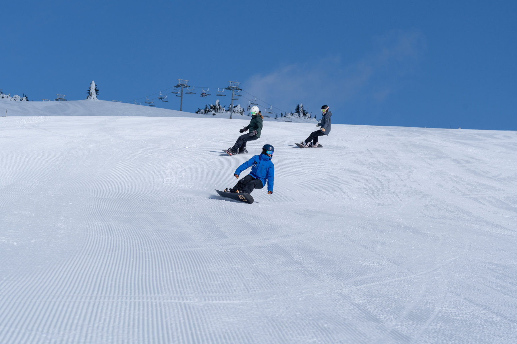 Three snowboarders on a freshly grommed run with blue sky