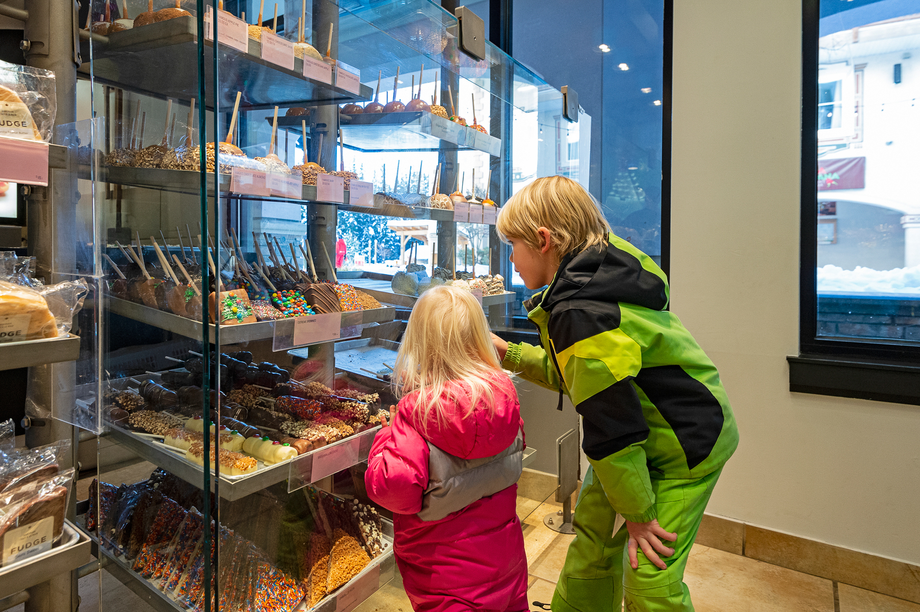 Children staring at candle through a glass wall in a candy shop