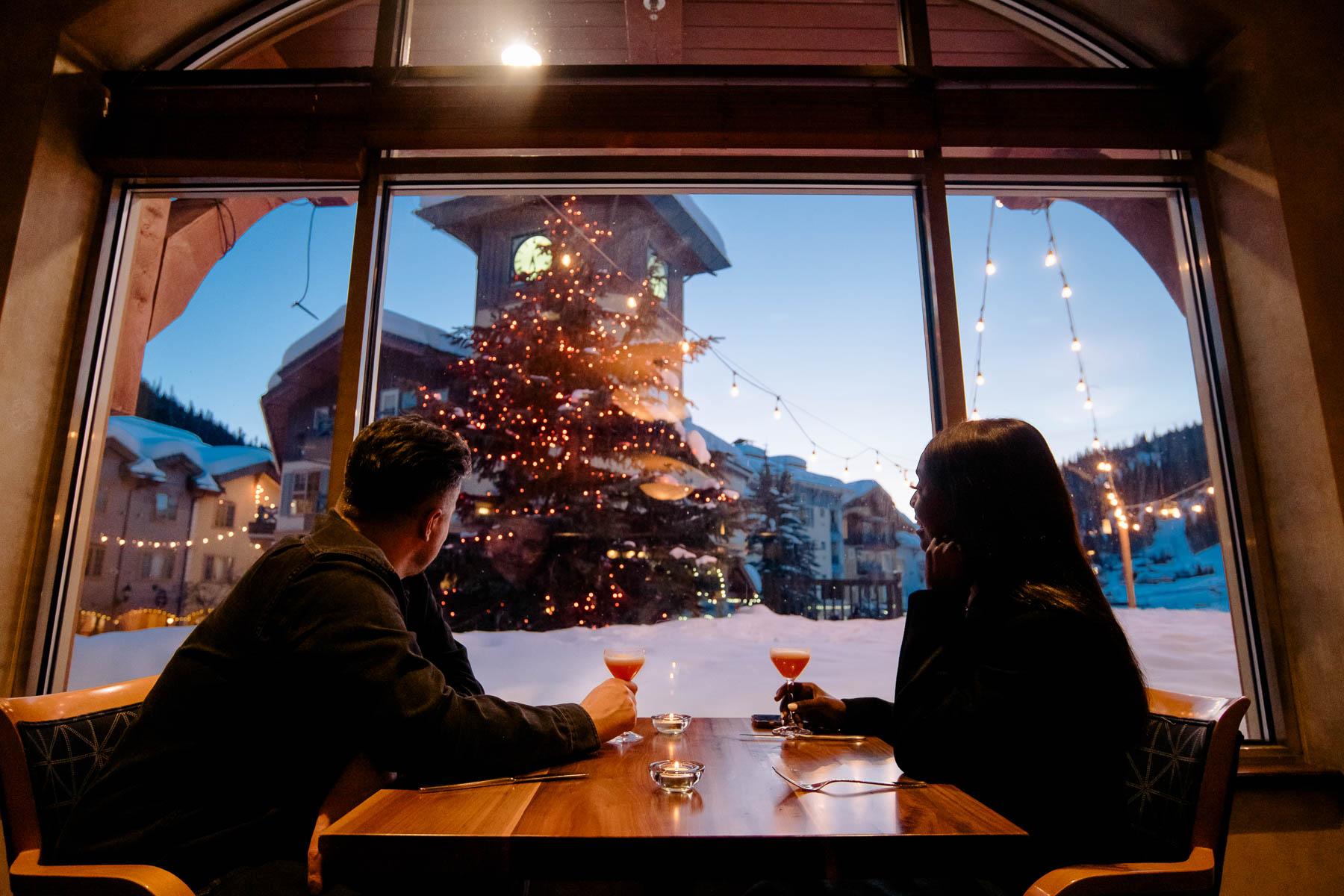 Two people staring out a window while sitting at a dining table having drinks