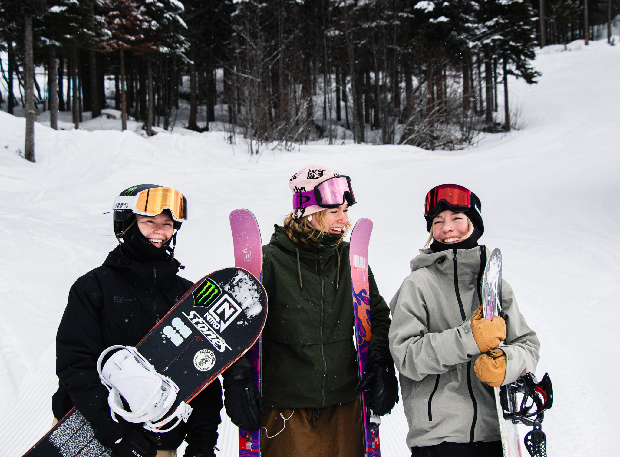 Three women snowboarders and skiers smiling in front of a snowy background