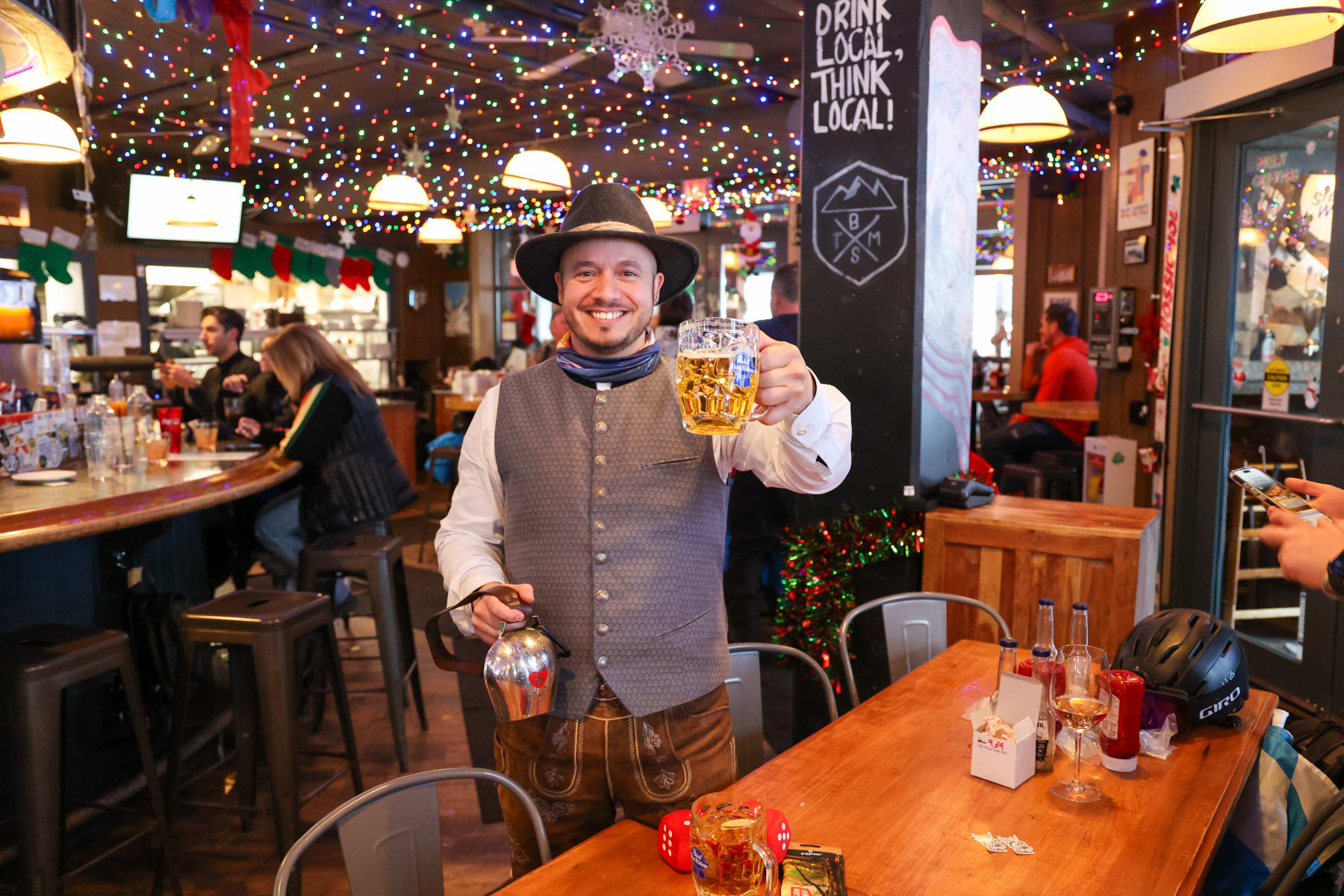 Ilkay in German traditional clothing holding a stein of beer and a bell for Apres Bells at Bottoms Bar, Sun Peaks.