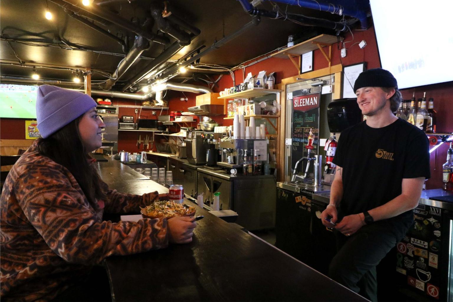 a woman sitting at the bar eating while talking with the staff behind the bar