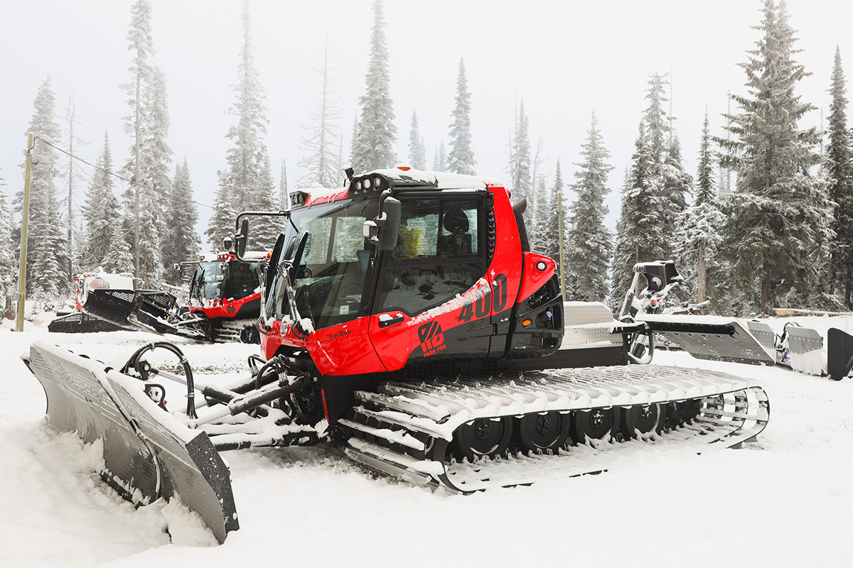 two red snow cats sit in a snow covered parking lot 