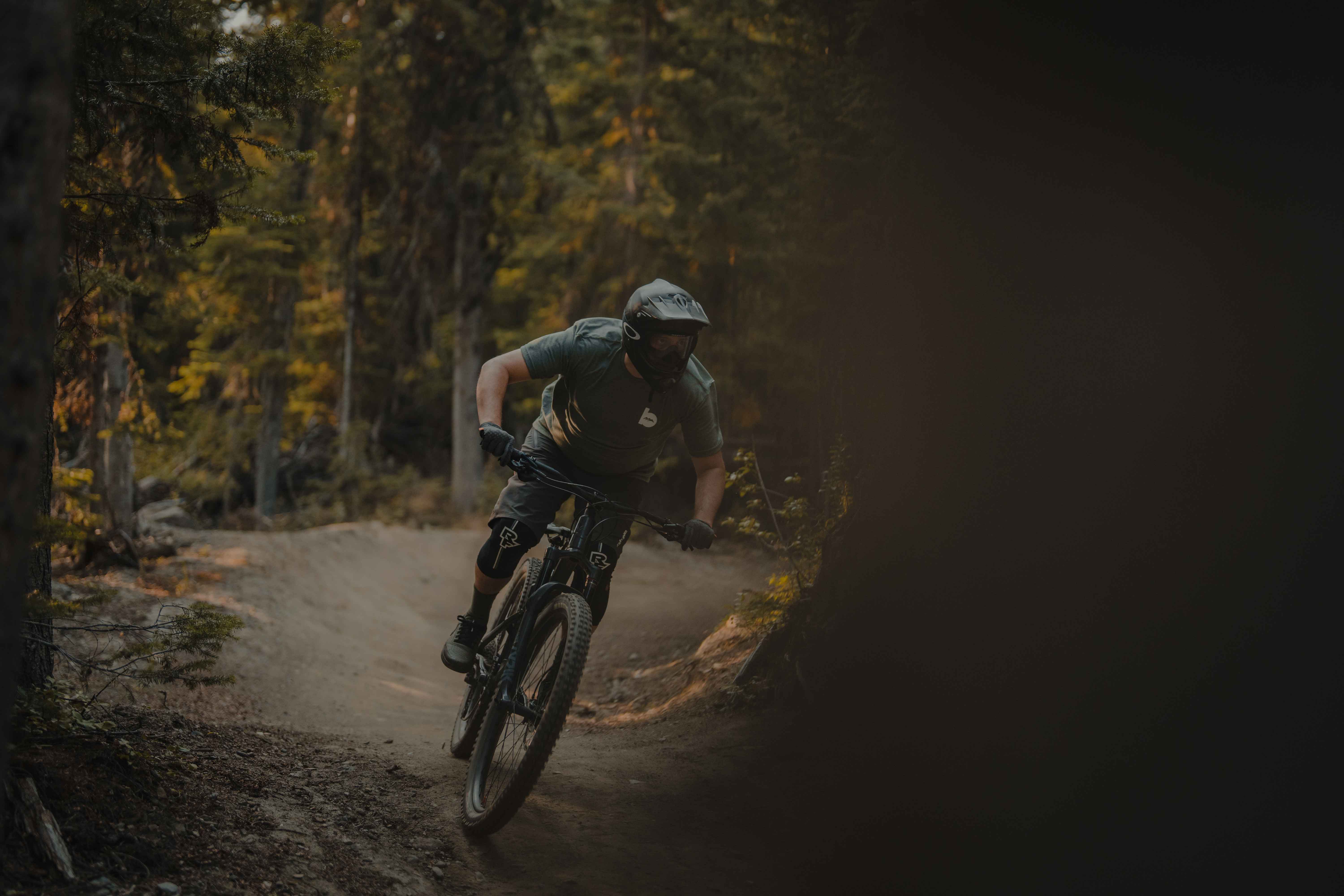 Downhill mountain biker riding a flow trail through a dimly lit forest. 
