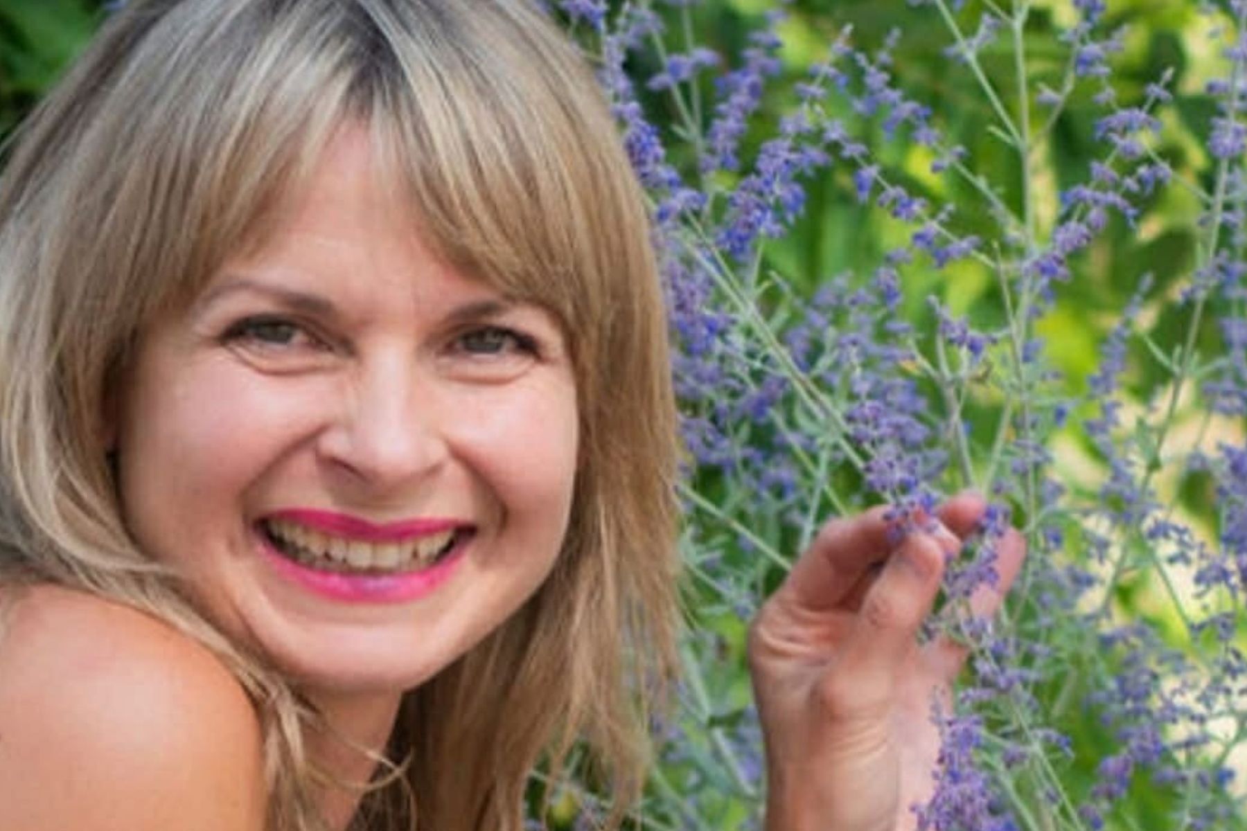 Angie smiling and holding purple flowers on a green outdoor background.