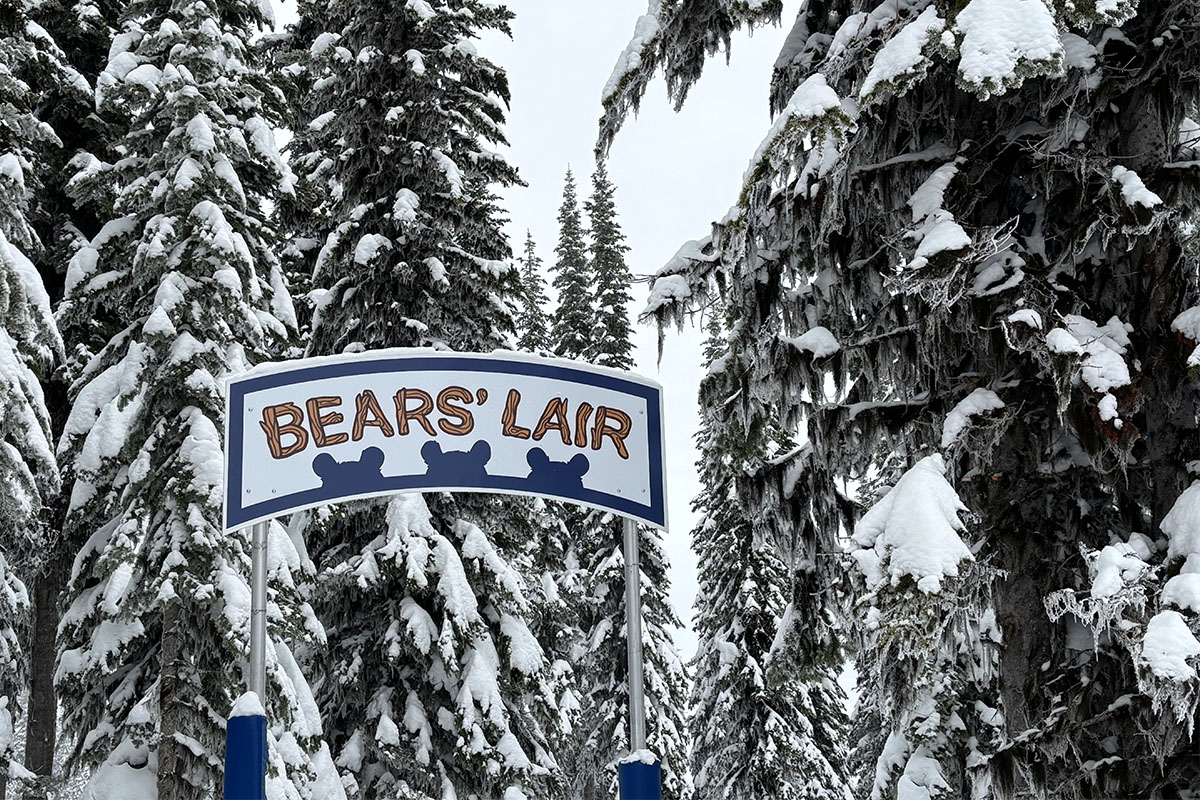 Sign for Bears' Lair secret entrance off of Sundance run between snowy trees.