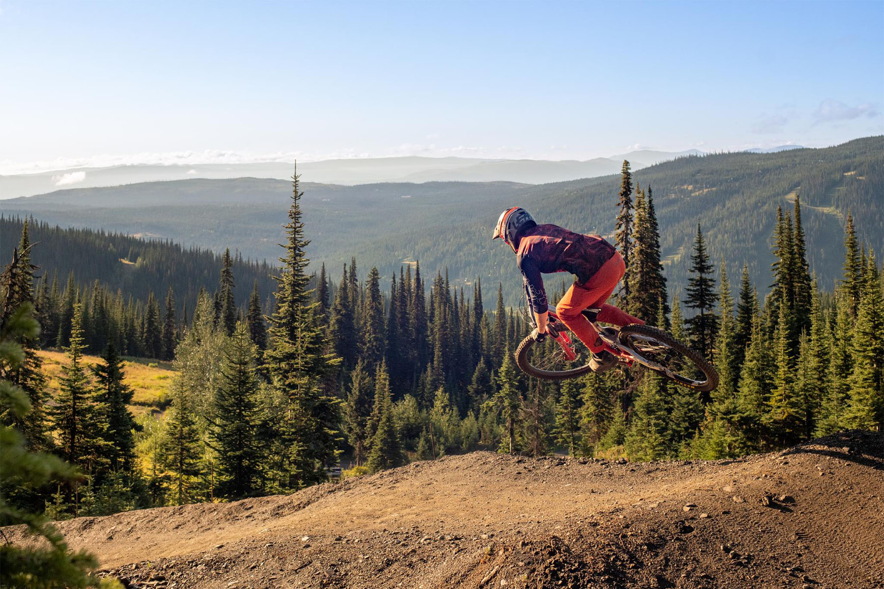 Mountain biker doing a jump, high above a green forested valley.
