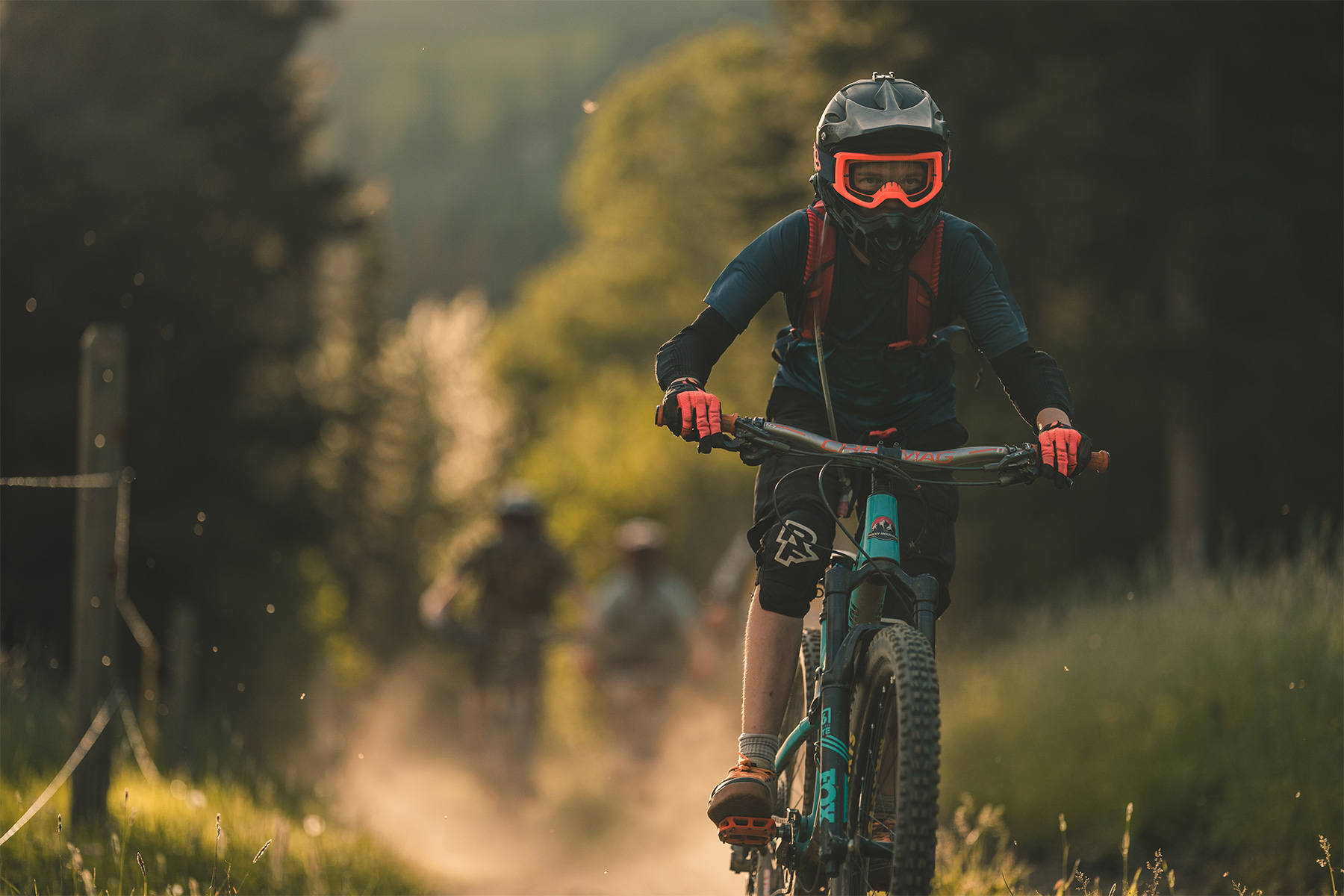 Mountain bikers riding down trail with dust lingering in the sunlight