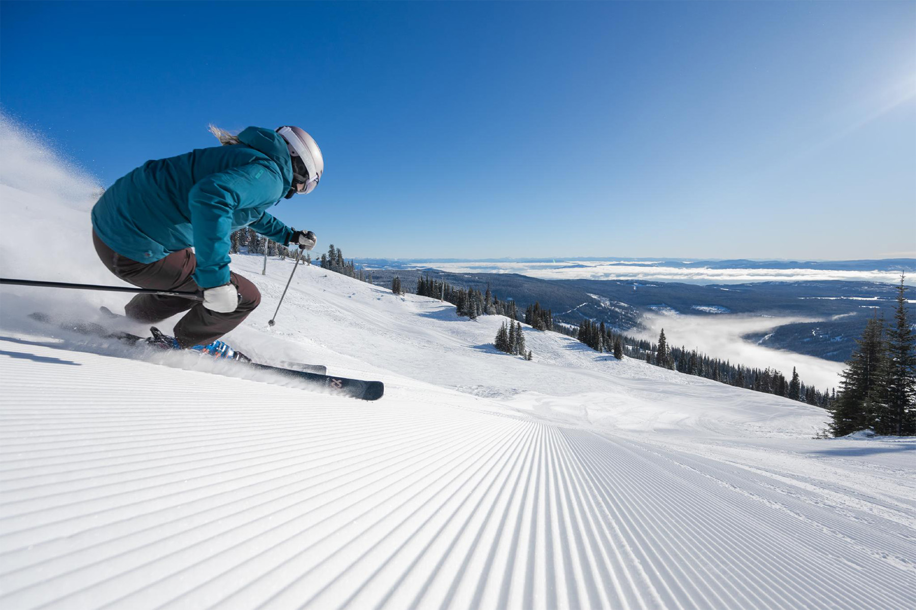 Skier making a fast turn on corduroy on a bluebird day.