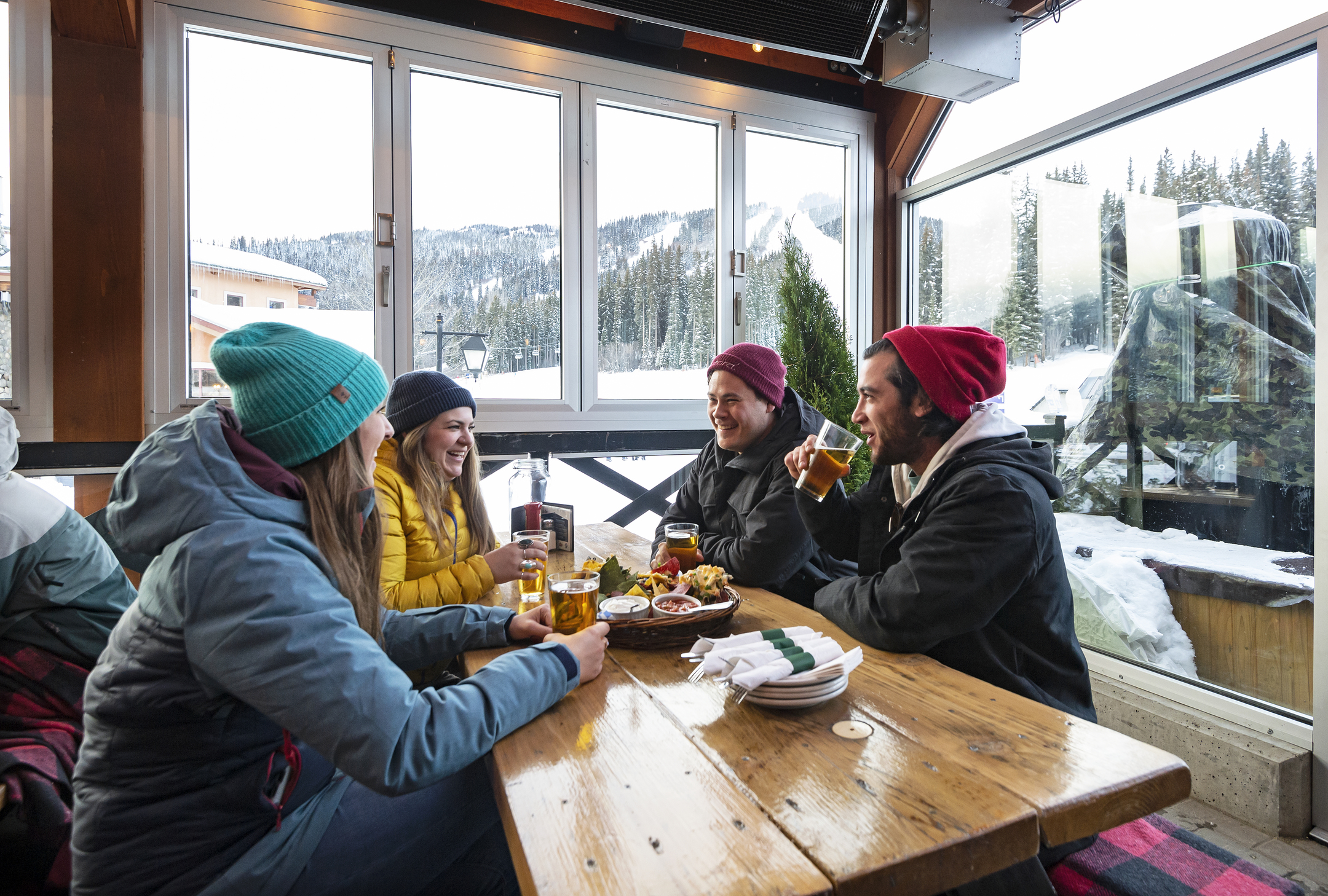 Four friends in winter jackets and hats enjoy après snacks and drinks at Mantles in Sun Peaks.