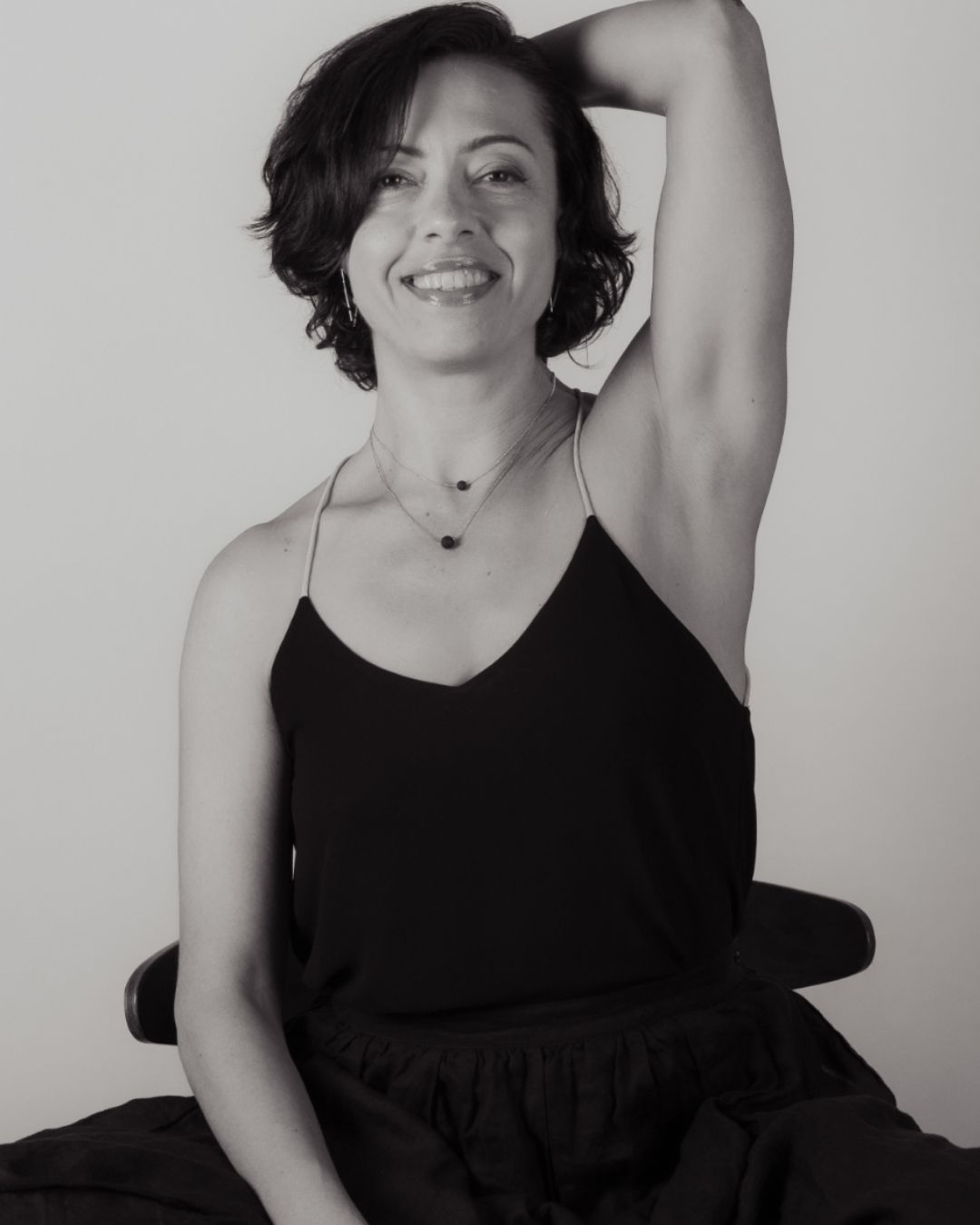 Dana Skoglund in a black tank top with short hair and an arm behind her head. Black and white shot.