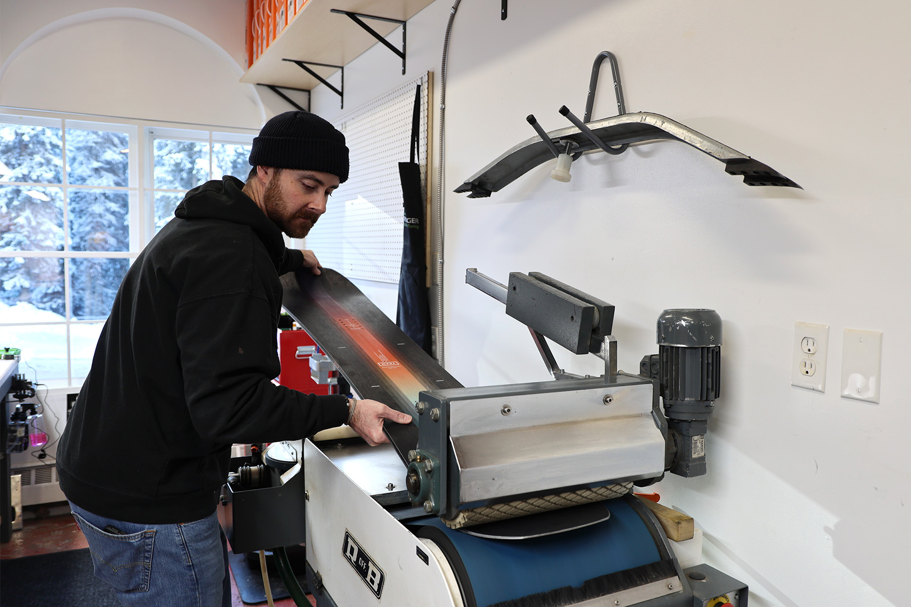 A man puts a snowboard through a waxing machine at District Ski in Sun Peaks
