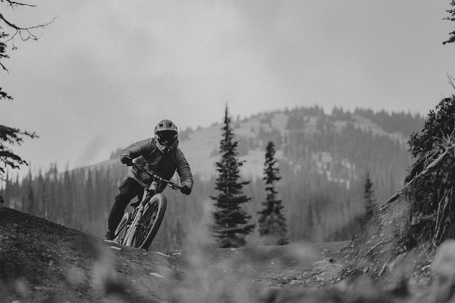 Black and white photo of mountain biker riding down a trail with mountain in background