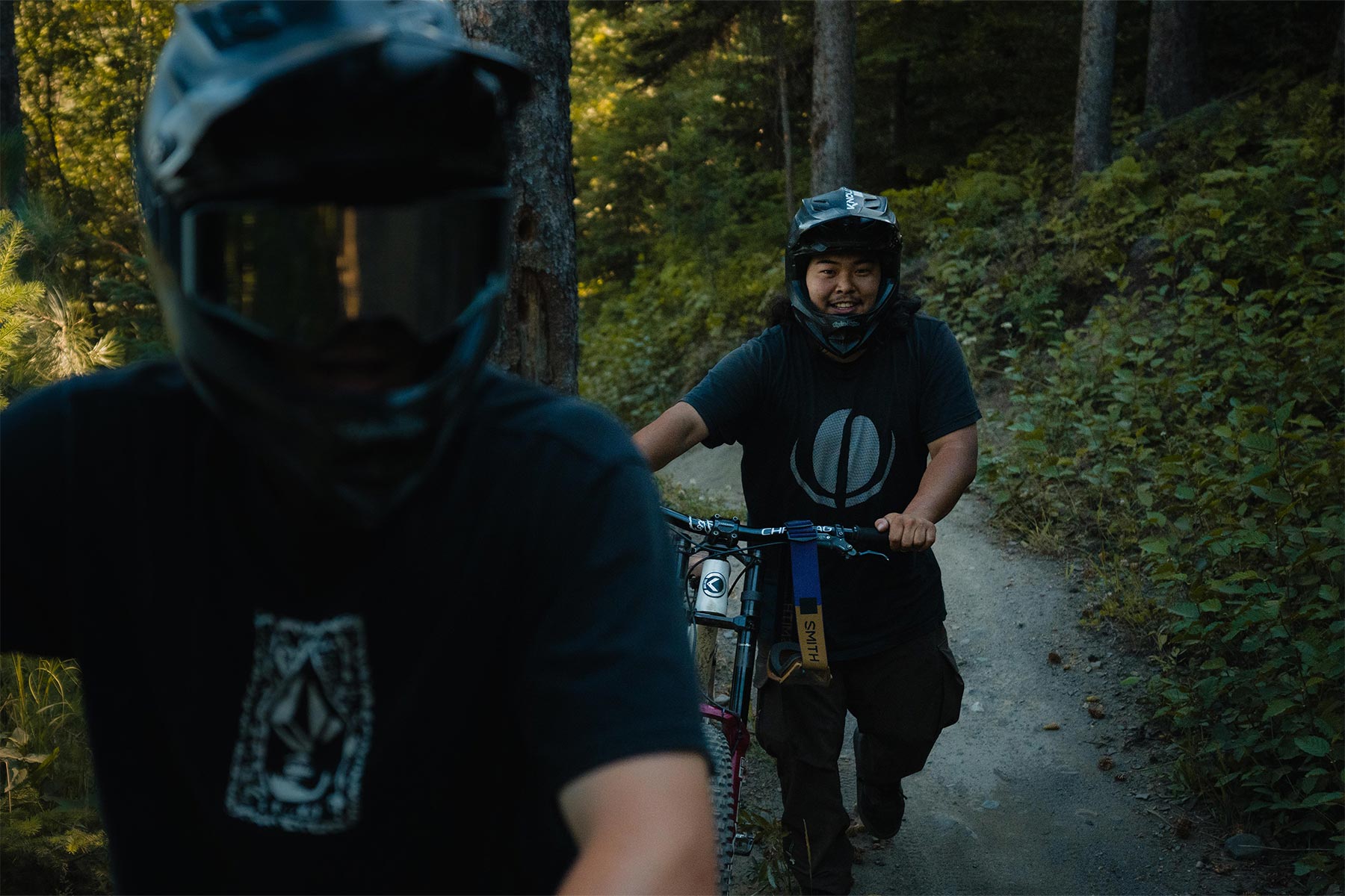 Two bikers walking their bikes in the trees