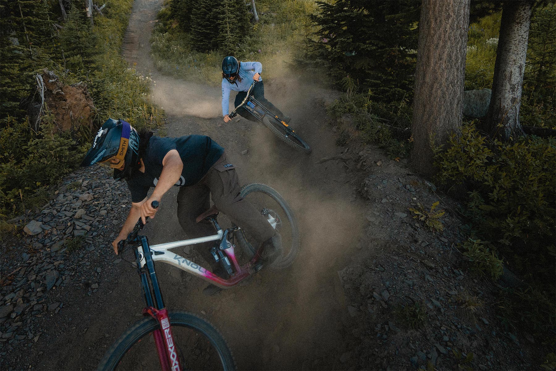 Two bikers riding a trail and turning a corner