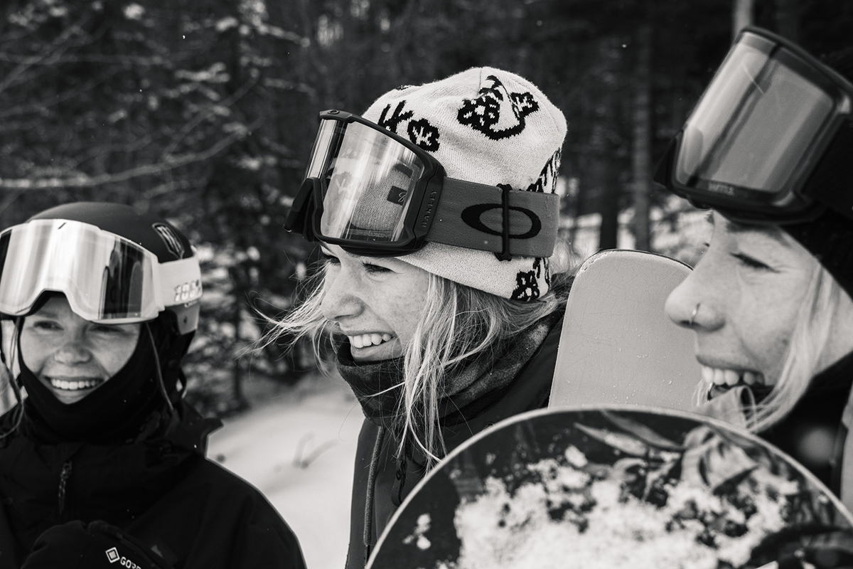Katie, Gabi, and Zuzy smiling with goggles on heads, in black and white, as viewed from the side.