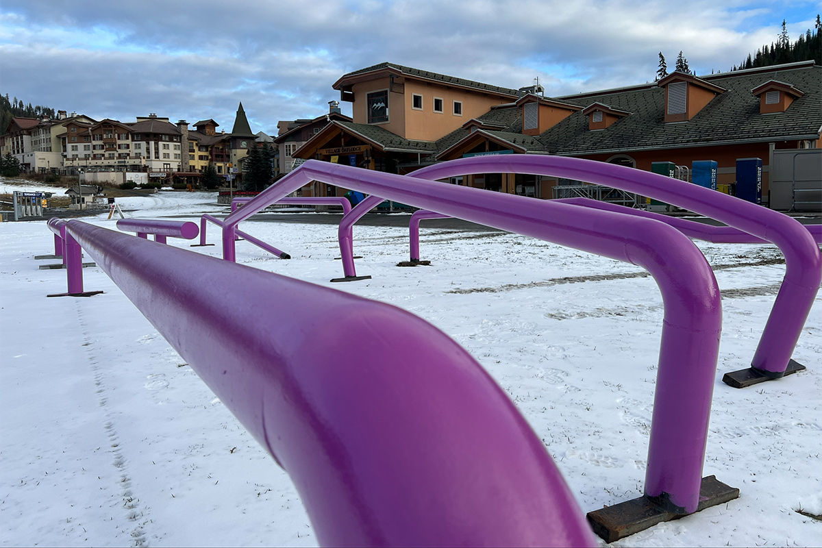 Magenta coloured terrain park rails sit in the lightly snow-covered Village, waiting to be installed. 