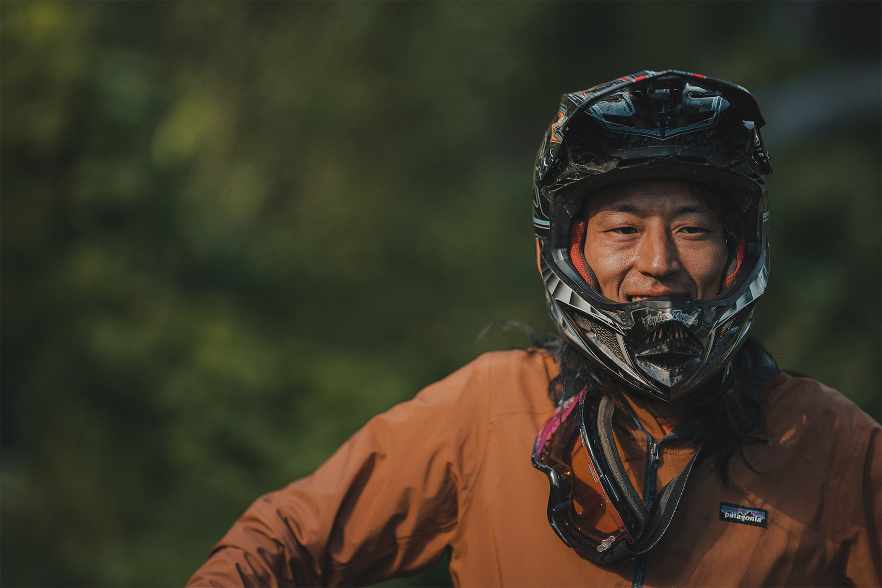 Mountain biker smiling at the camera with helmet on and goggles around their neck