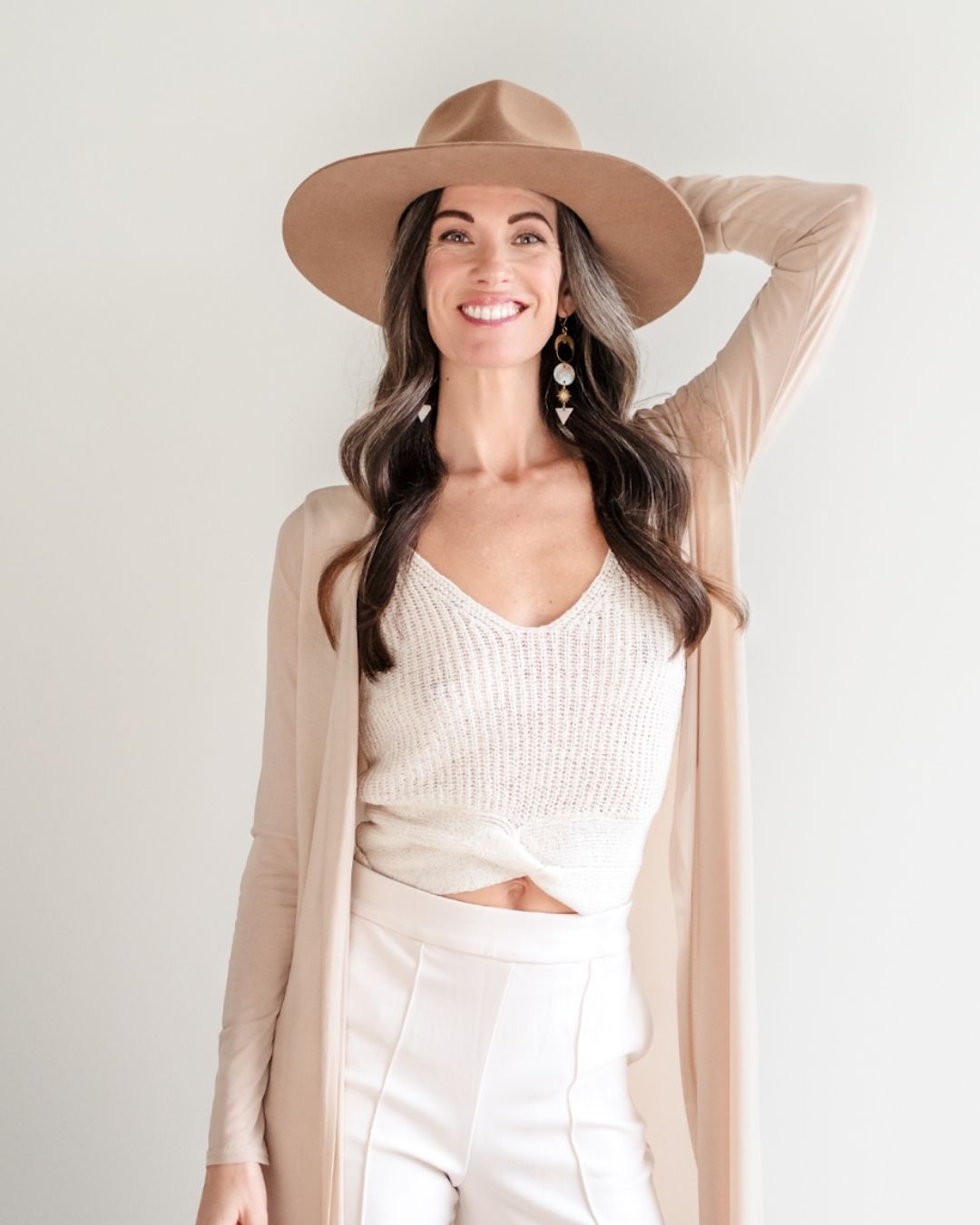 Jenn Pike smiling in a light tan and white outfit with hat and arm lifted up behind her head.