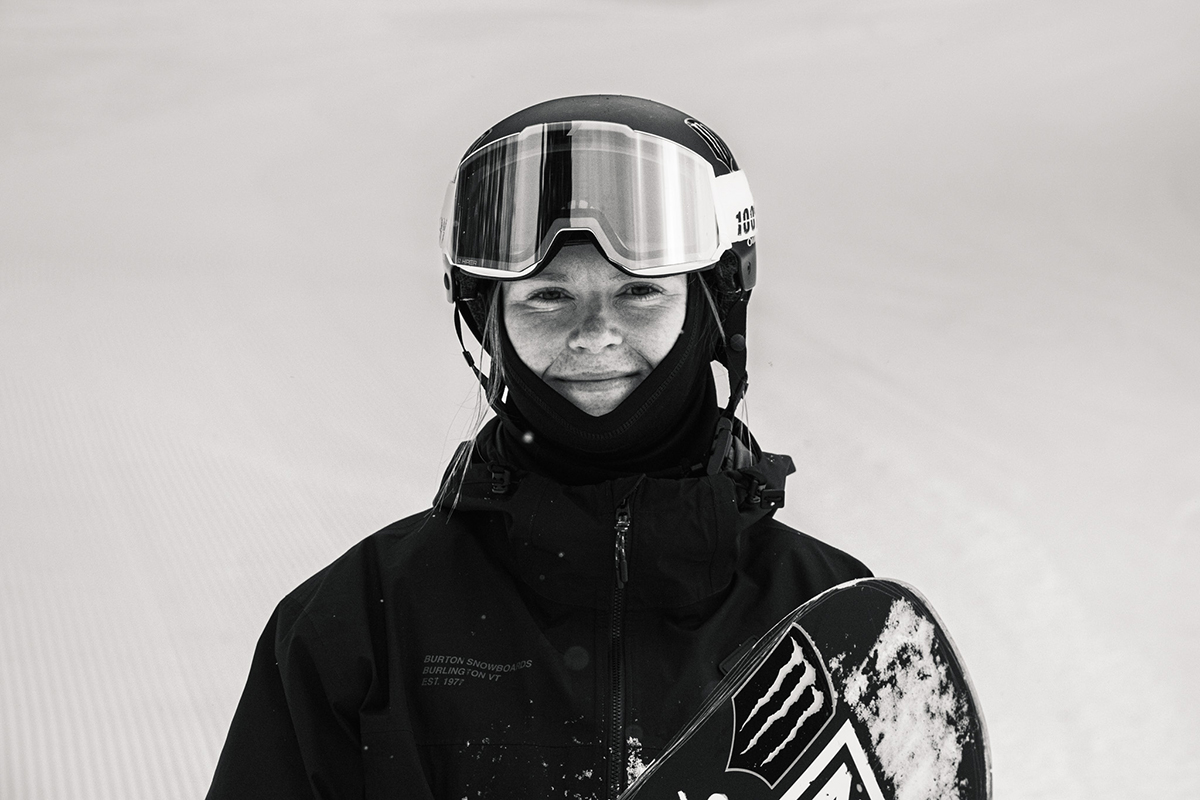 Katie Brayer smiles at camera while holding snowboard.