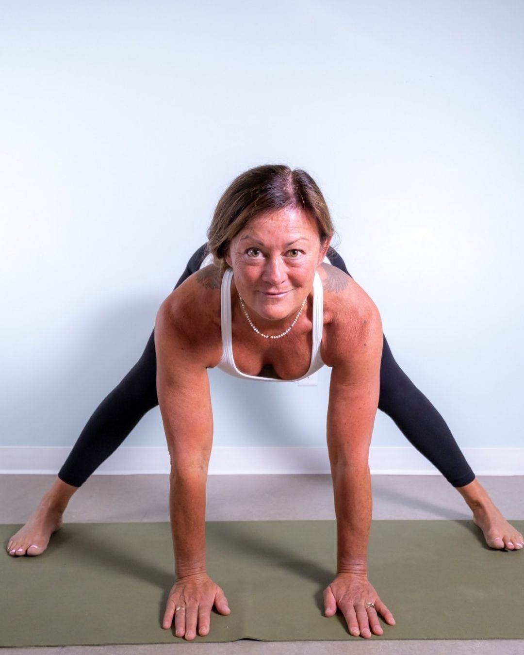 Kelly Craig in a folded over yoga position, head towards the camera and smiling.