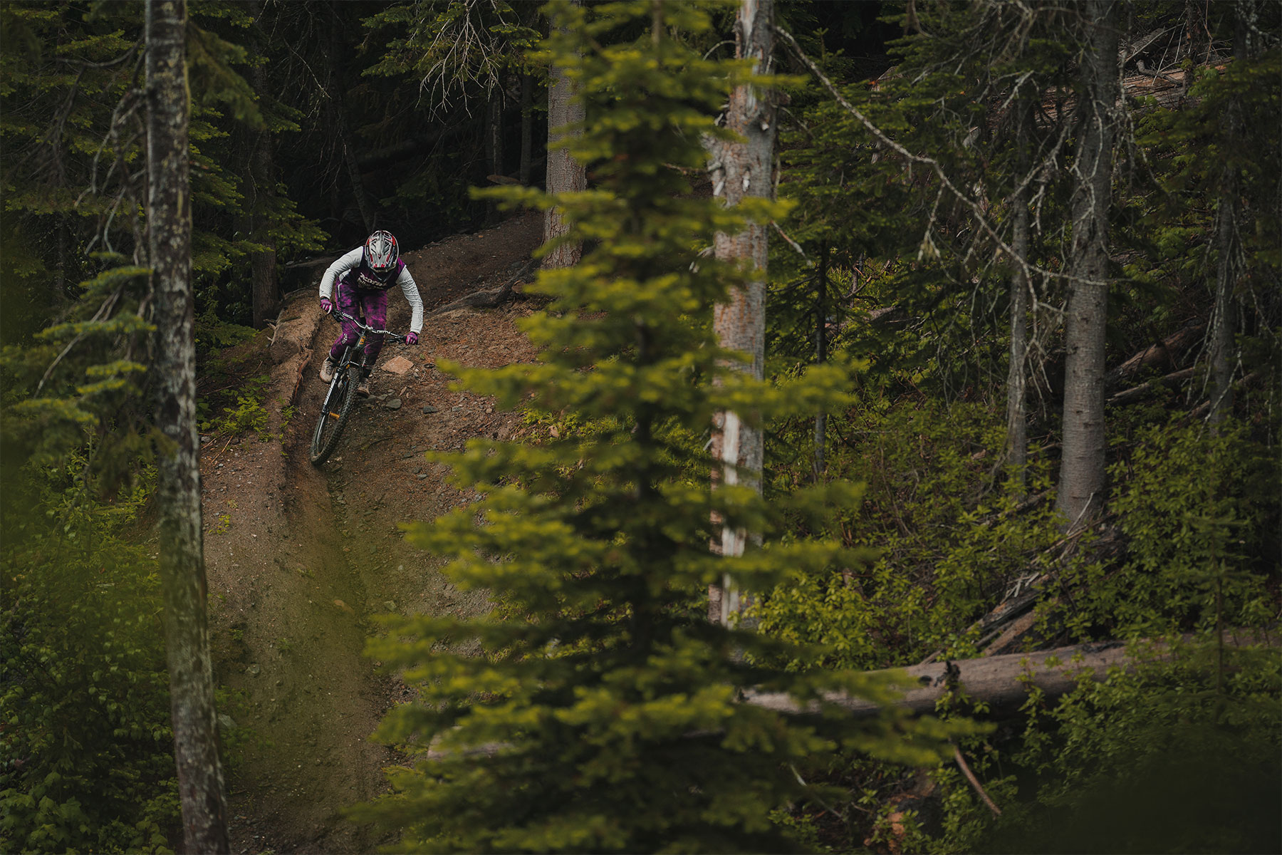 Kyleigh riding down a steep tech trail with lush green foliage surrounding it