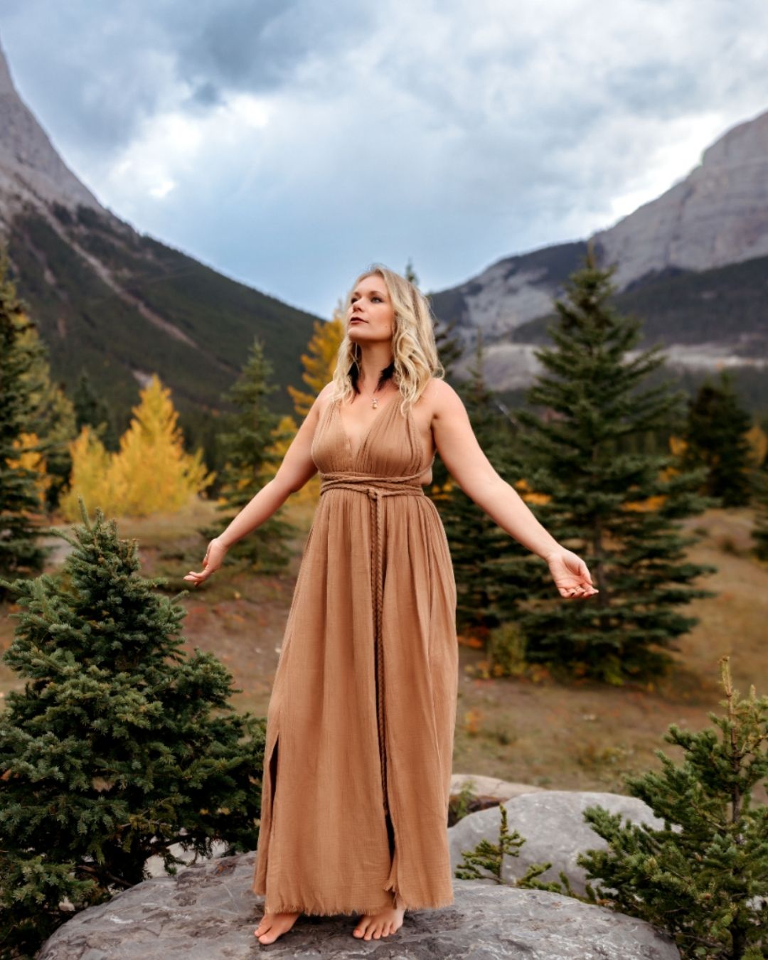 Meaghan Alton wearing a long brown dress in a mountain environment, arms outstretched.