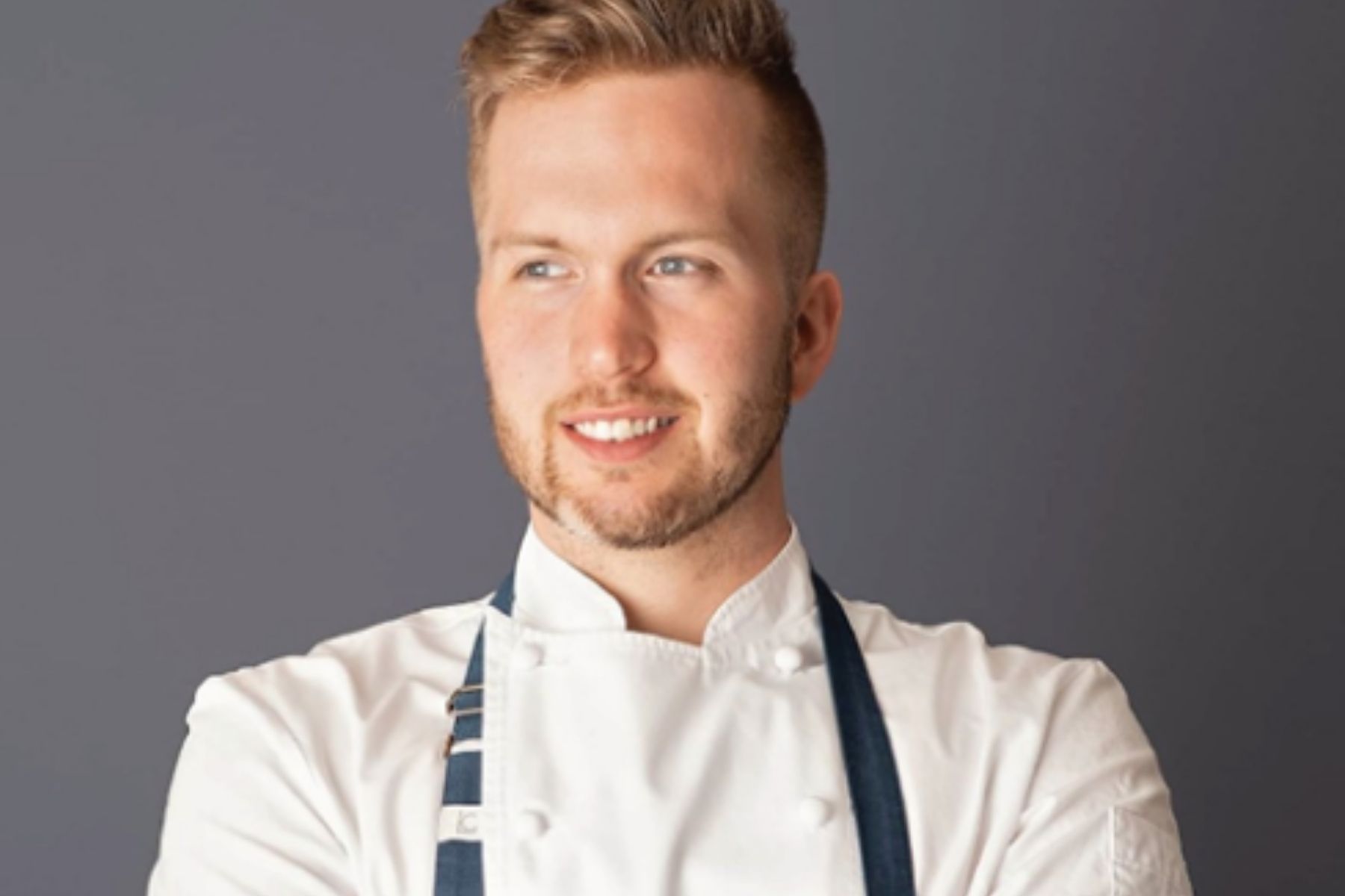 Chef Michael Roszell smiling and looking to the side on a grey background