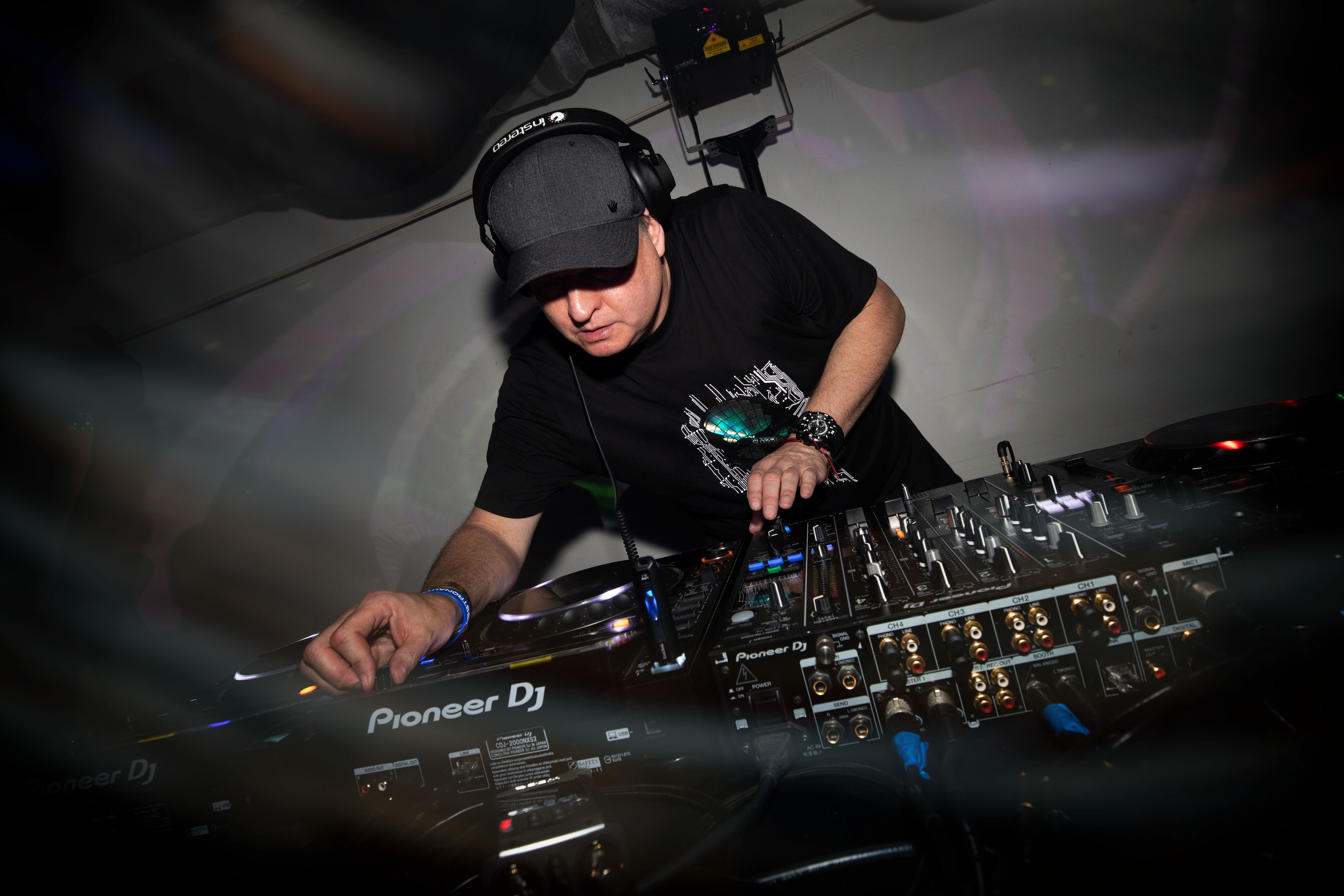 DJ Dan spinning records on a large record table with a ballcap and black shirt on.