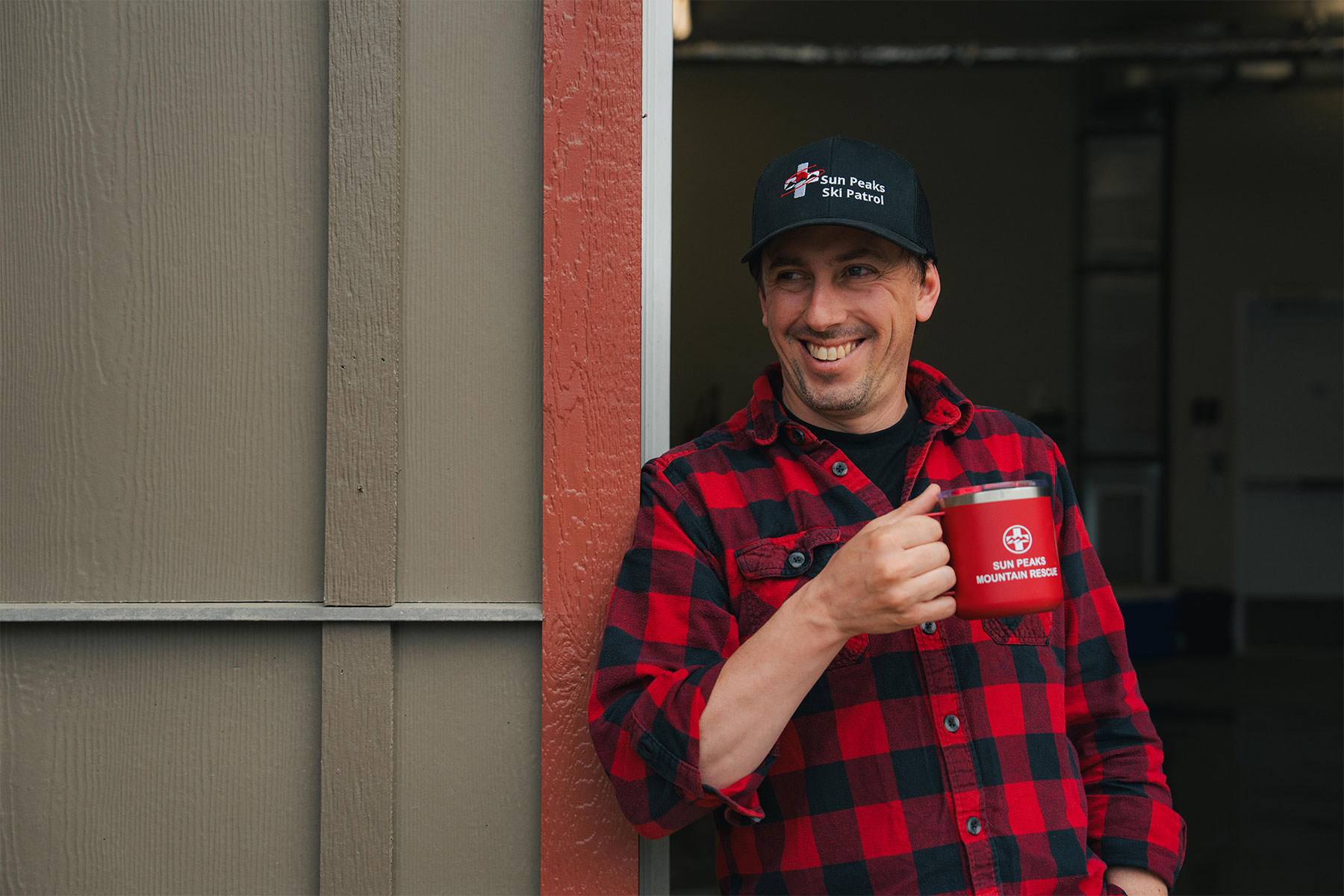 Man standing against a wall holding a coffee cup smiling
