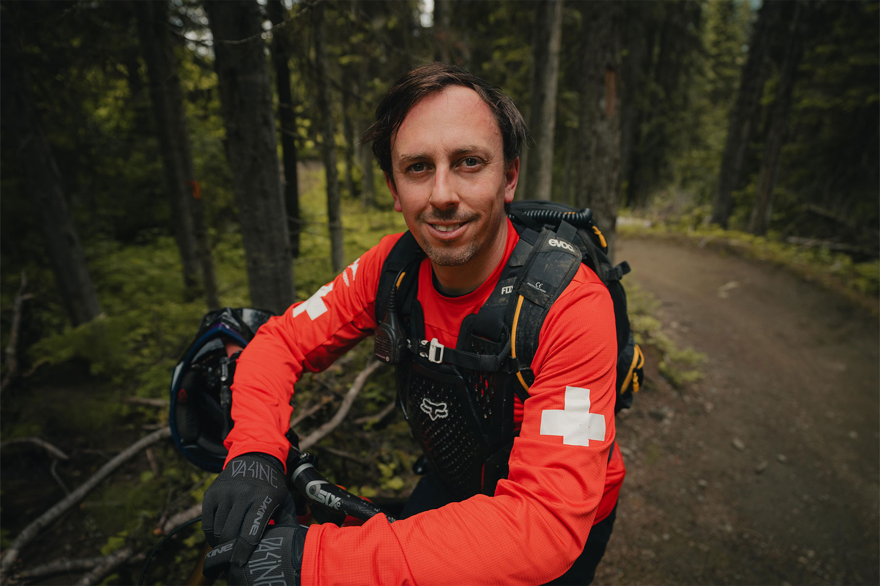 Bike Park patroller smiling at the camera with greenery behind him.