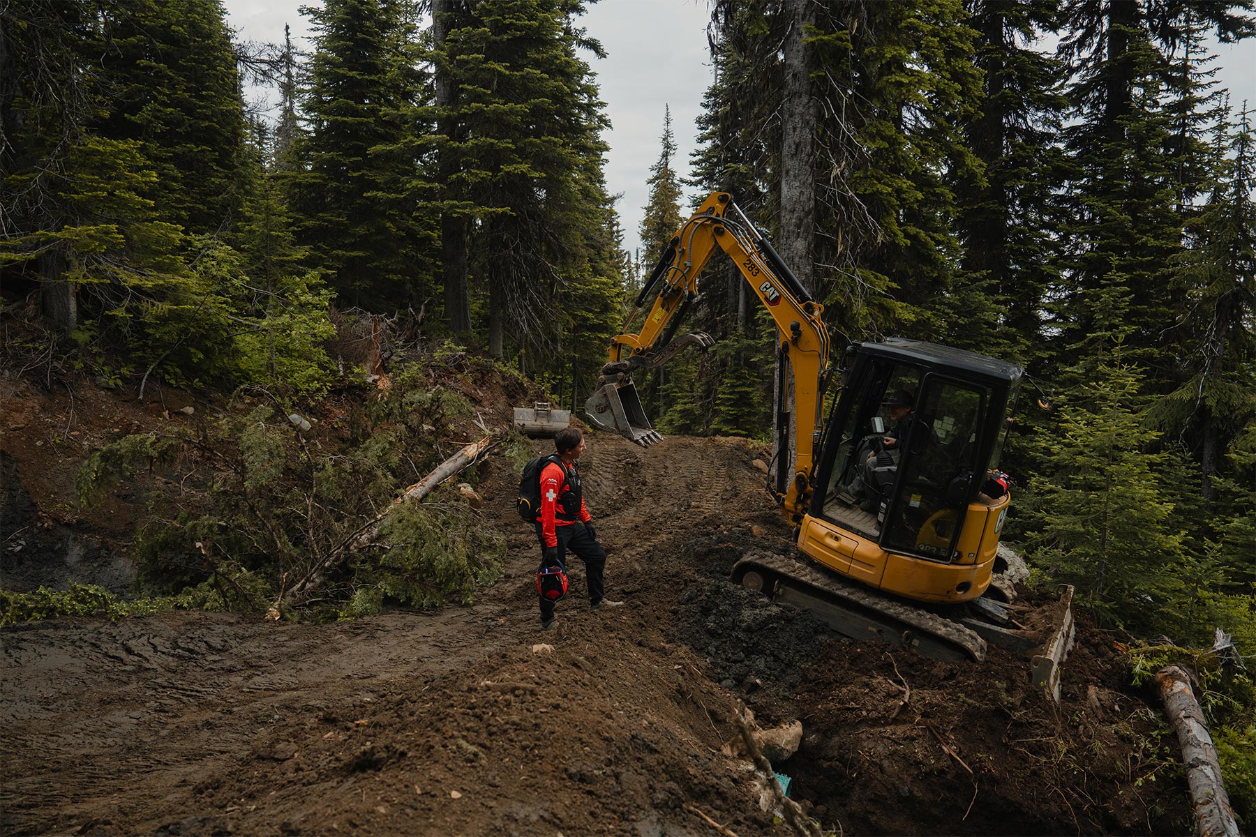 Patroller standing beside a tractor on a bike trail surrounded by trees.
