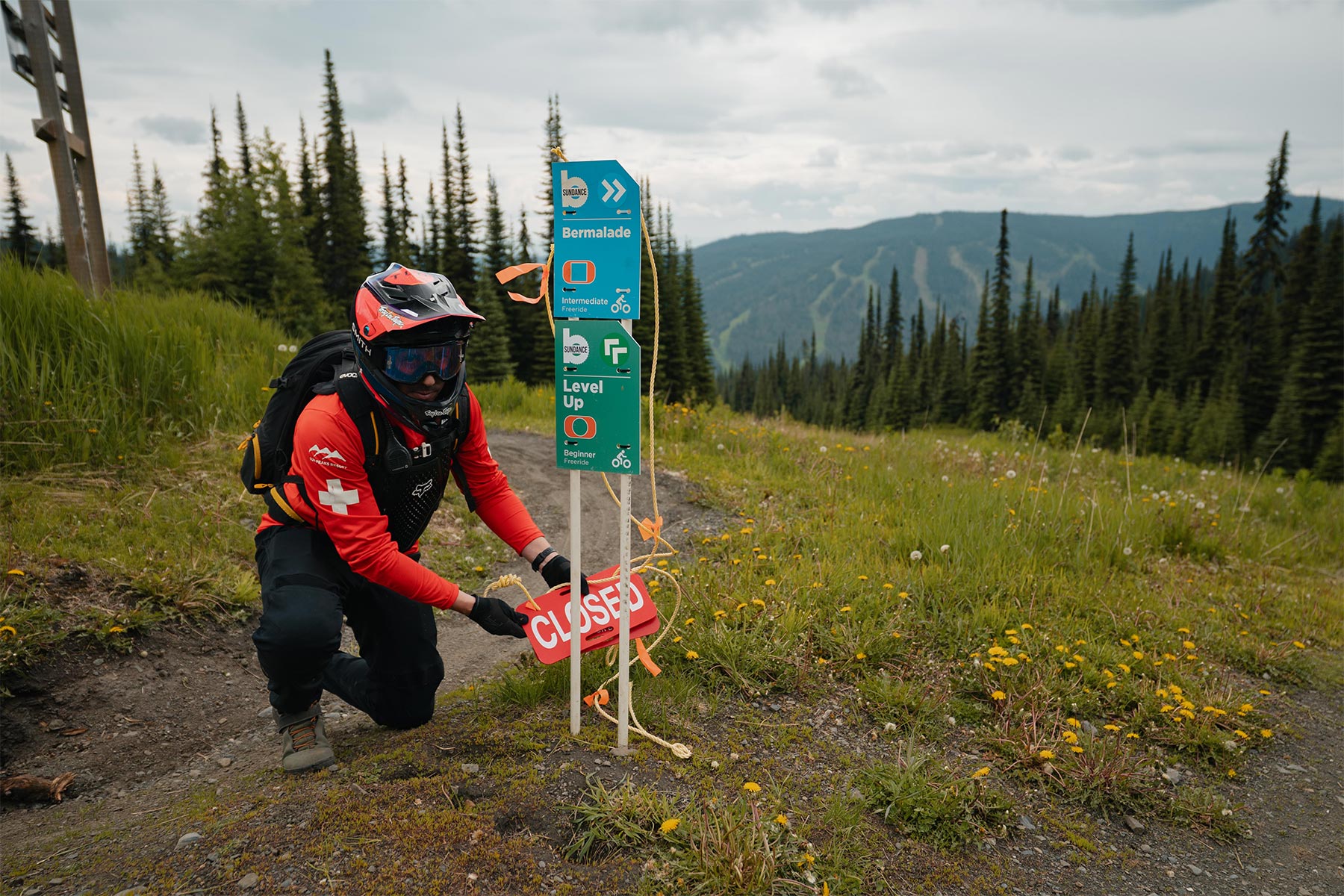 patroller fixing trail signs on the mountain with trees around him and mountain views