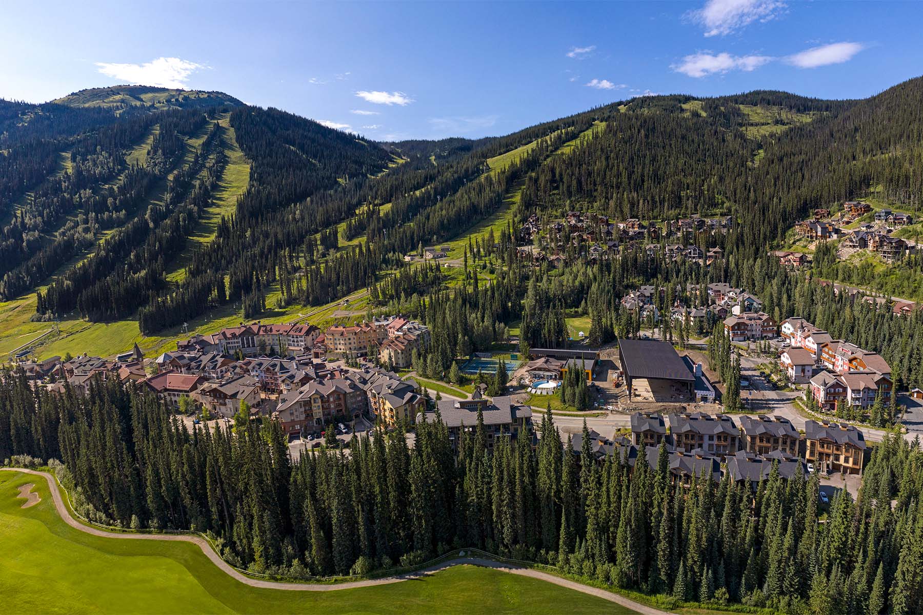 Sun Peaks village in summer time, nestled between green mountains and trees.