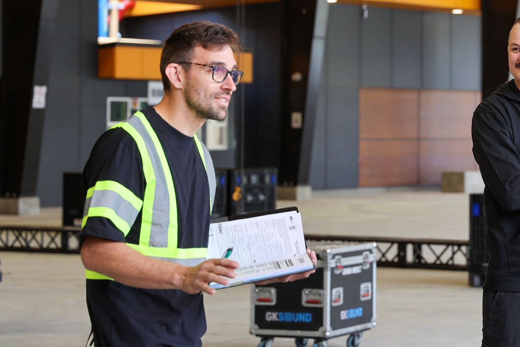 Man in a reflective vest in an event production environment with a clipboard.