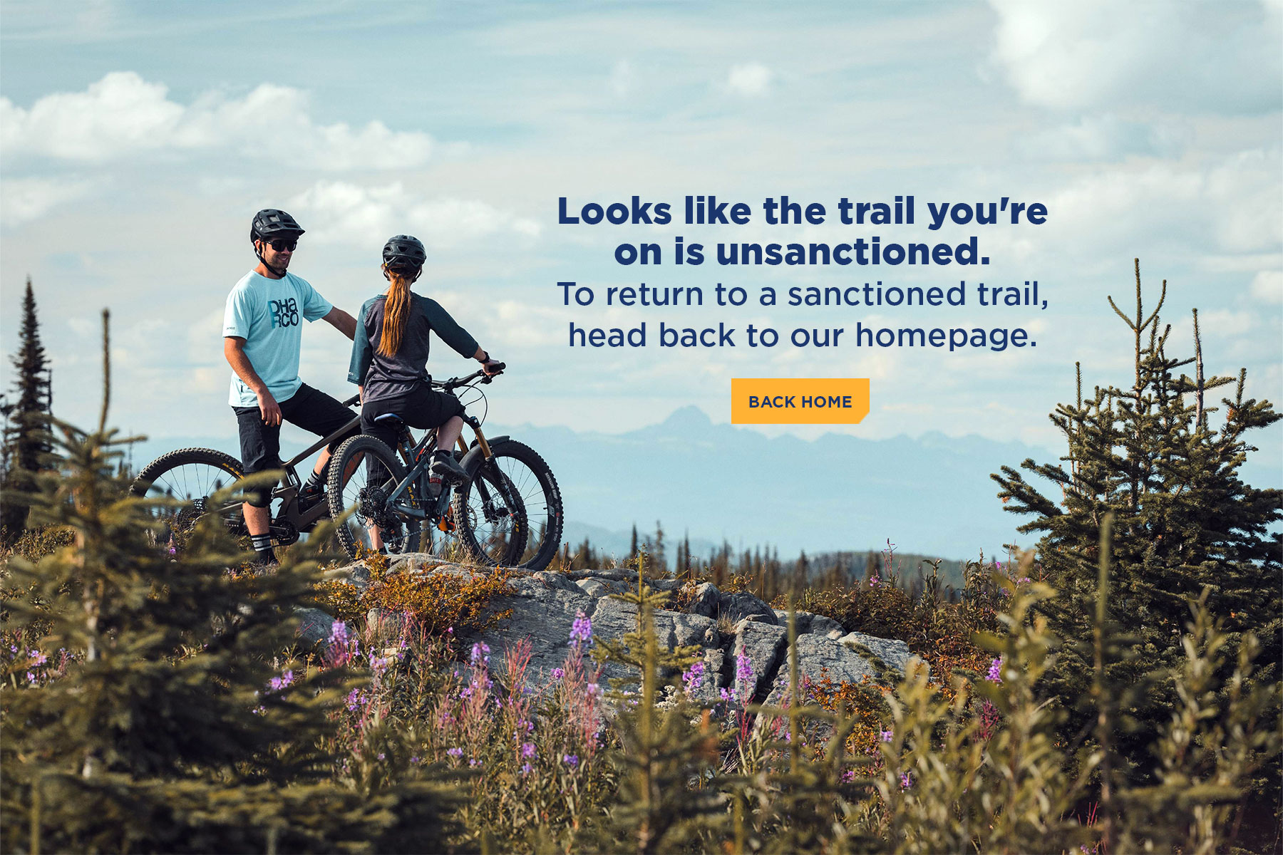 Two mountain bikers pause on a rocky alpine trail at Sun Peaks Resort, surrounded by wildflowers and mountain views. Text overlay reads, “Looks like the trail you’re on is unsanctioned. To return to a sanctioned trail, head back to our homepage.”