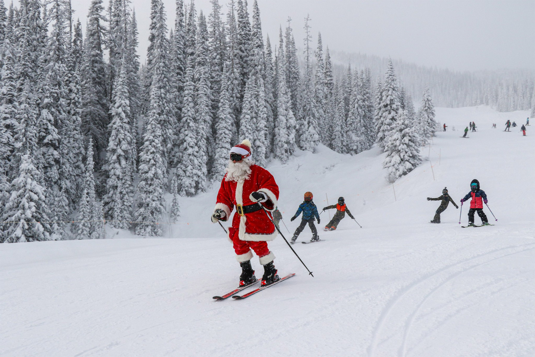 Santa skiing down the hill with children behind him