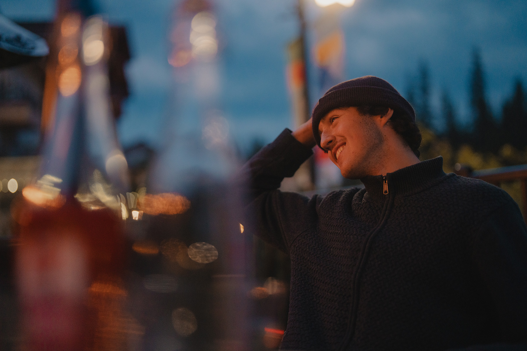 A man in a toque smiles while sitting on a patio at night.