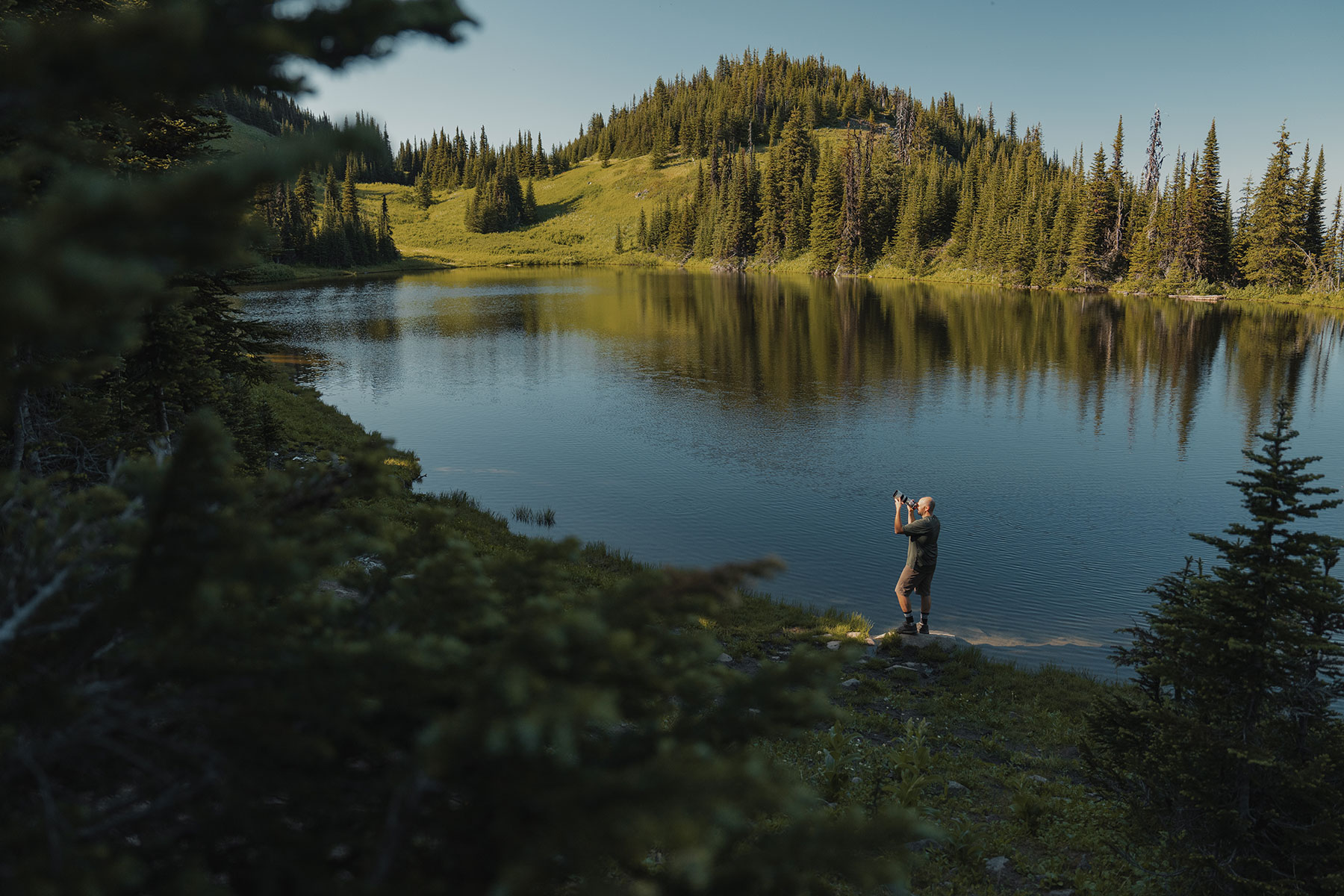 A photographer stands at an alpine lake. 