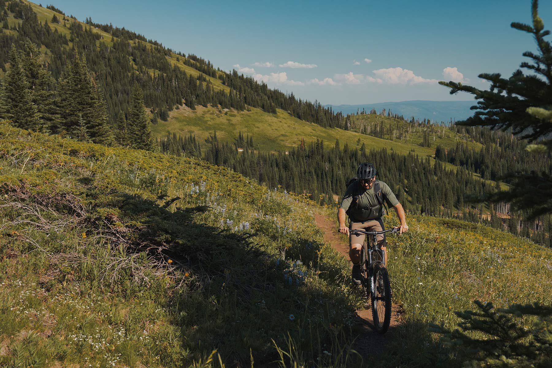 A mountain biker ascends an alpine trail with a camera bag on his back.
