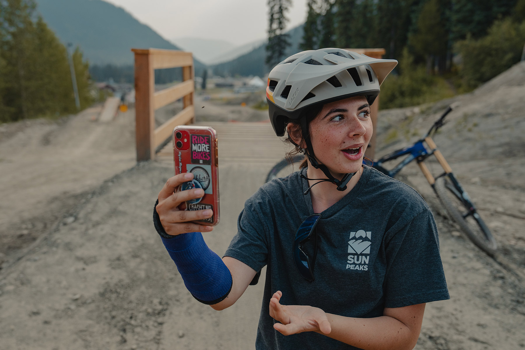 A girl with her wrist in a cast, holds her iPhone up to record a fellow mountain biker,