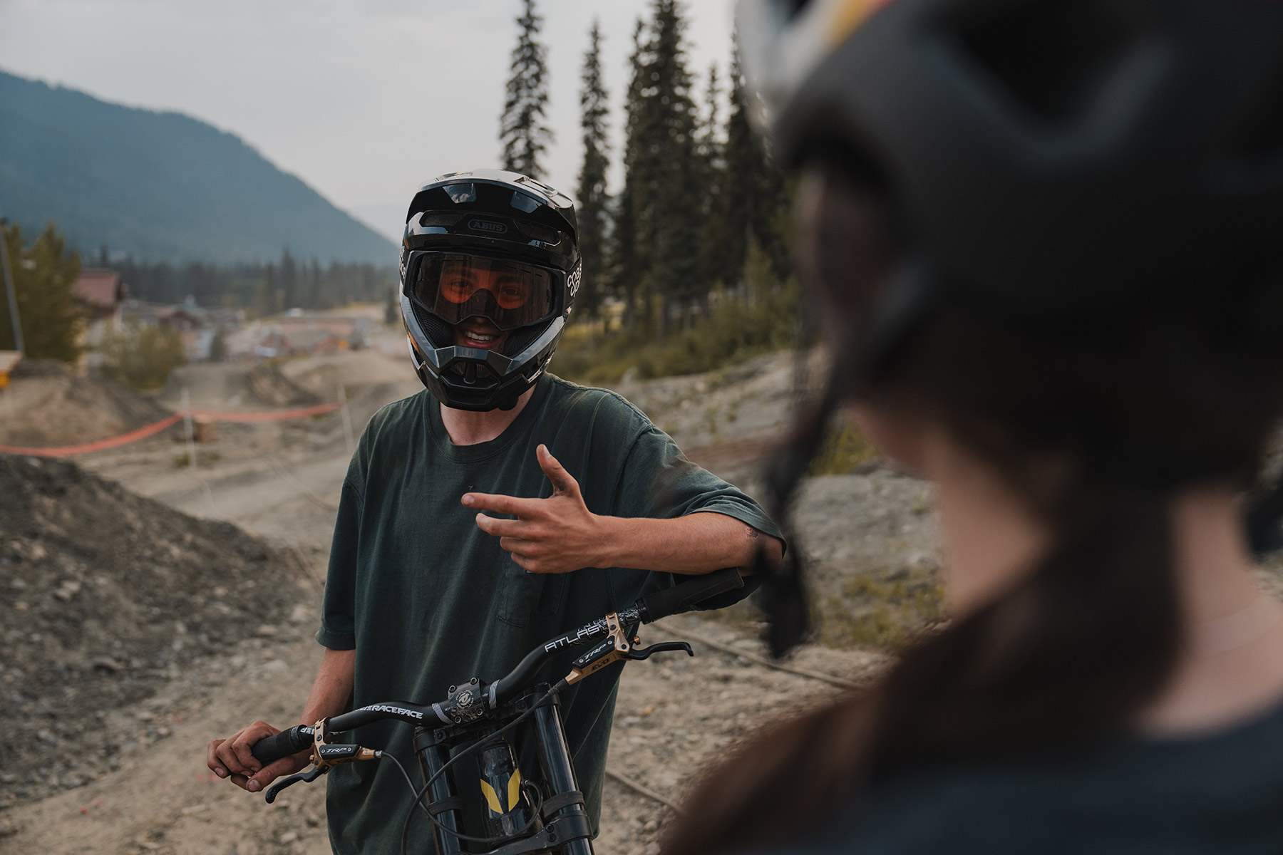 A mountain biker in a full-face DH helmet and goggles smiles at the camera.