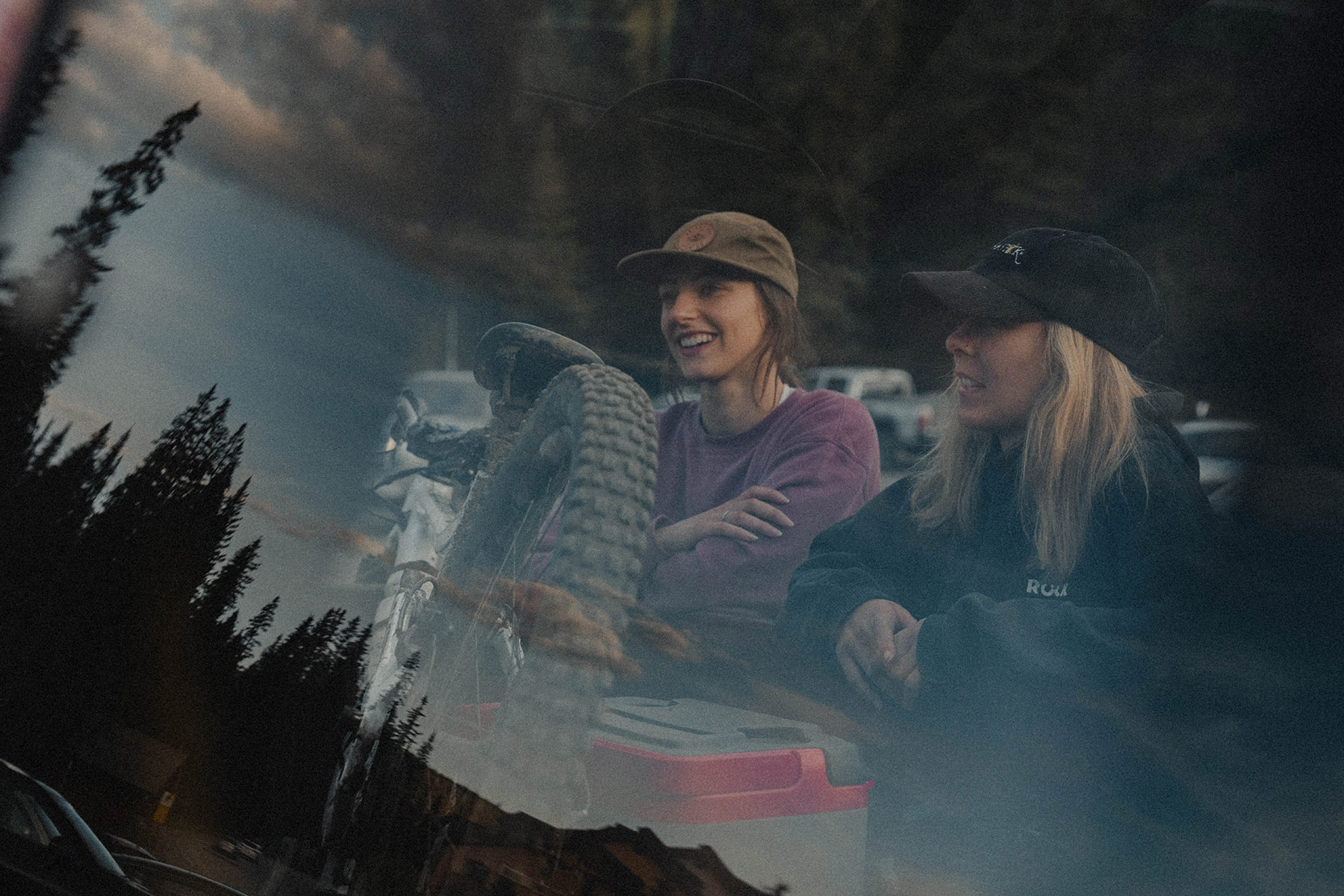 The window reflection of two women in baseball caps leaning over the truck bed.