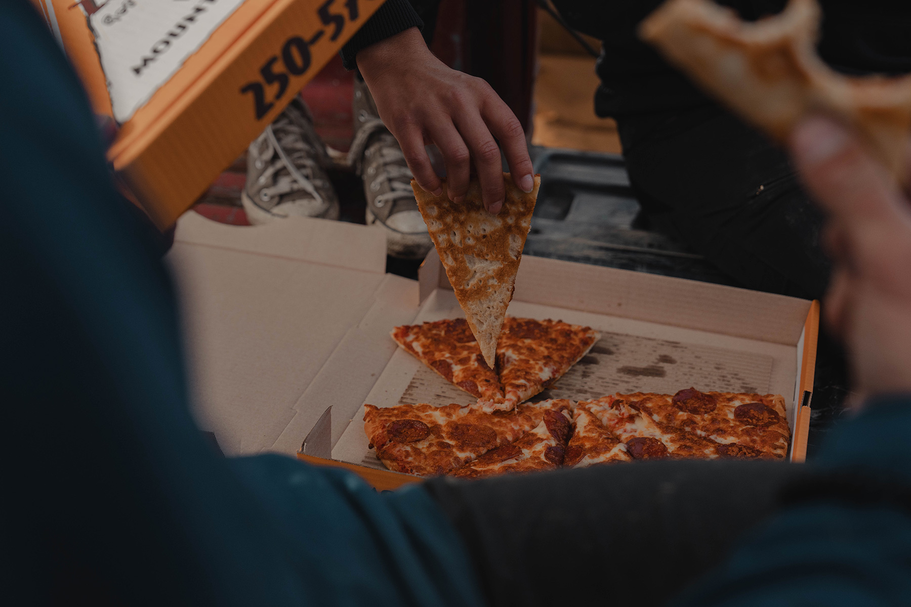 Pepperoni pizza slices are picked out of an orange pizza box.
