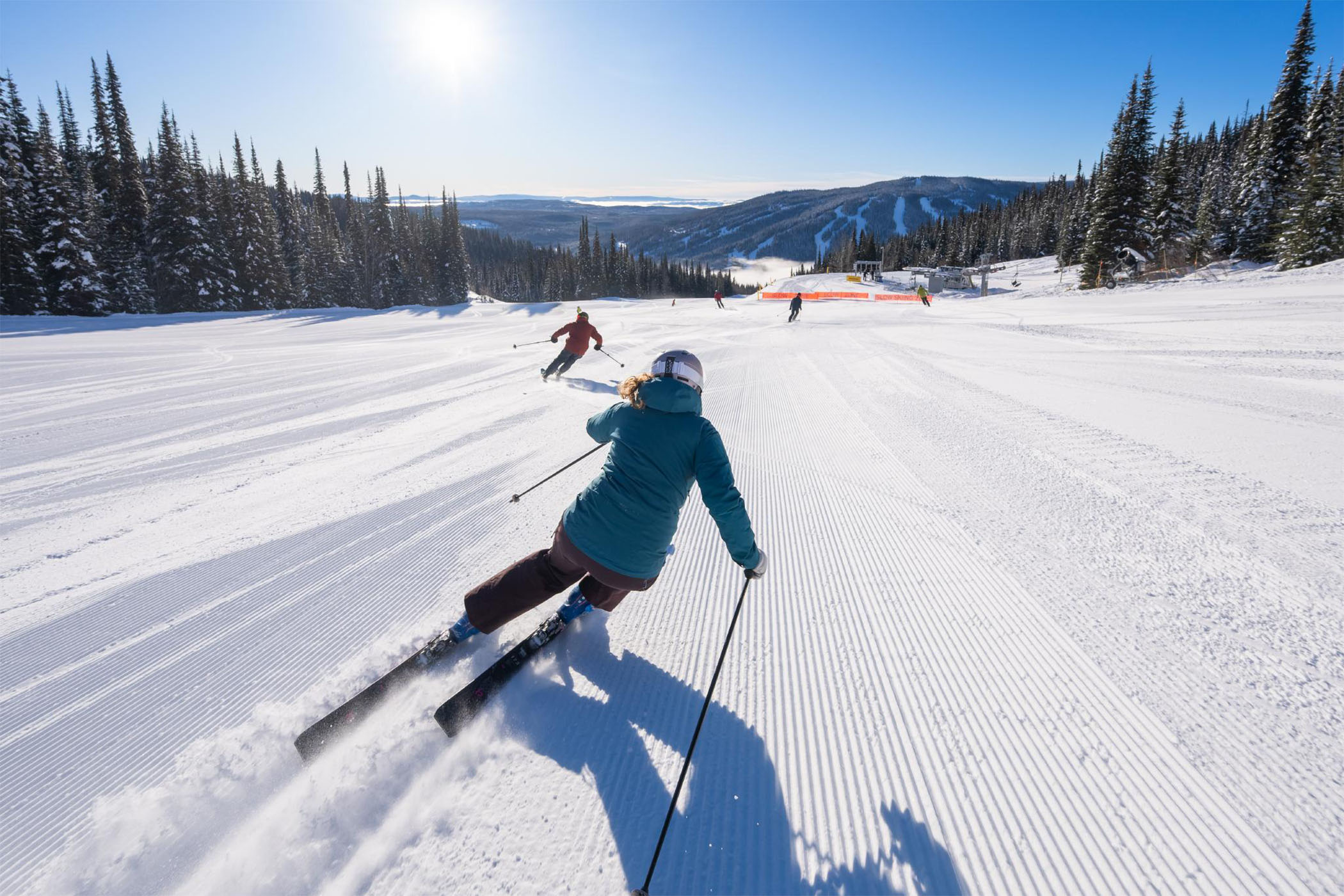 Couple of skiers on a freshly groomed run with a chairlift in front of them.
