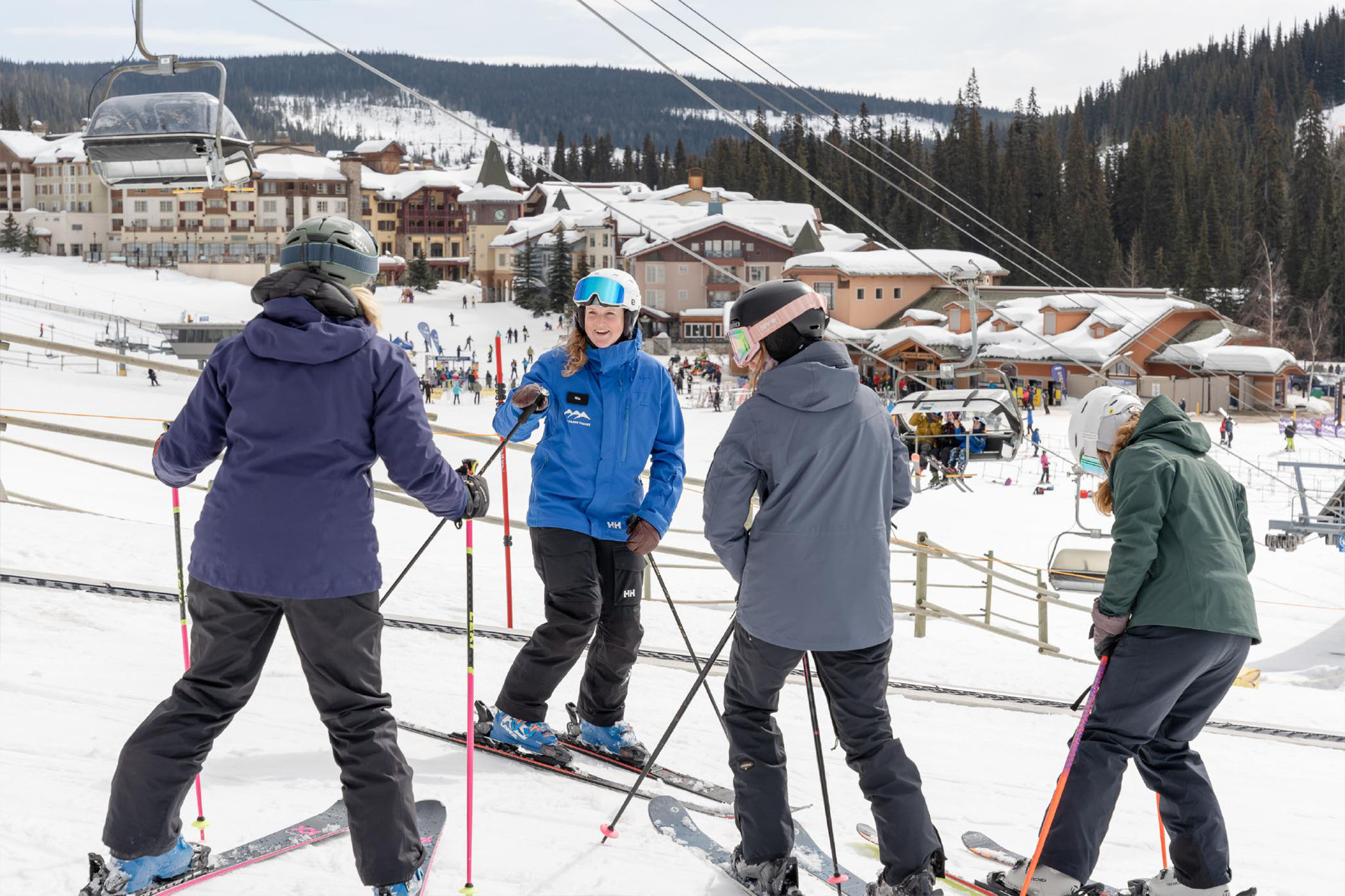 Ski instructor in a blue jacket gives a lesson to three beginner skiers in the Sun Peaks learning area. 