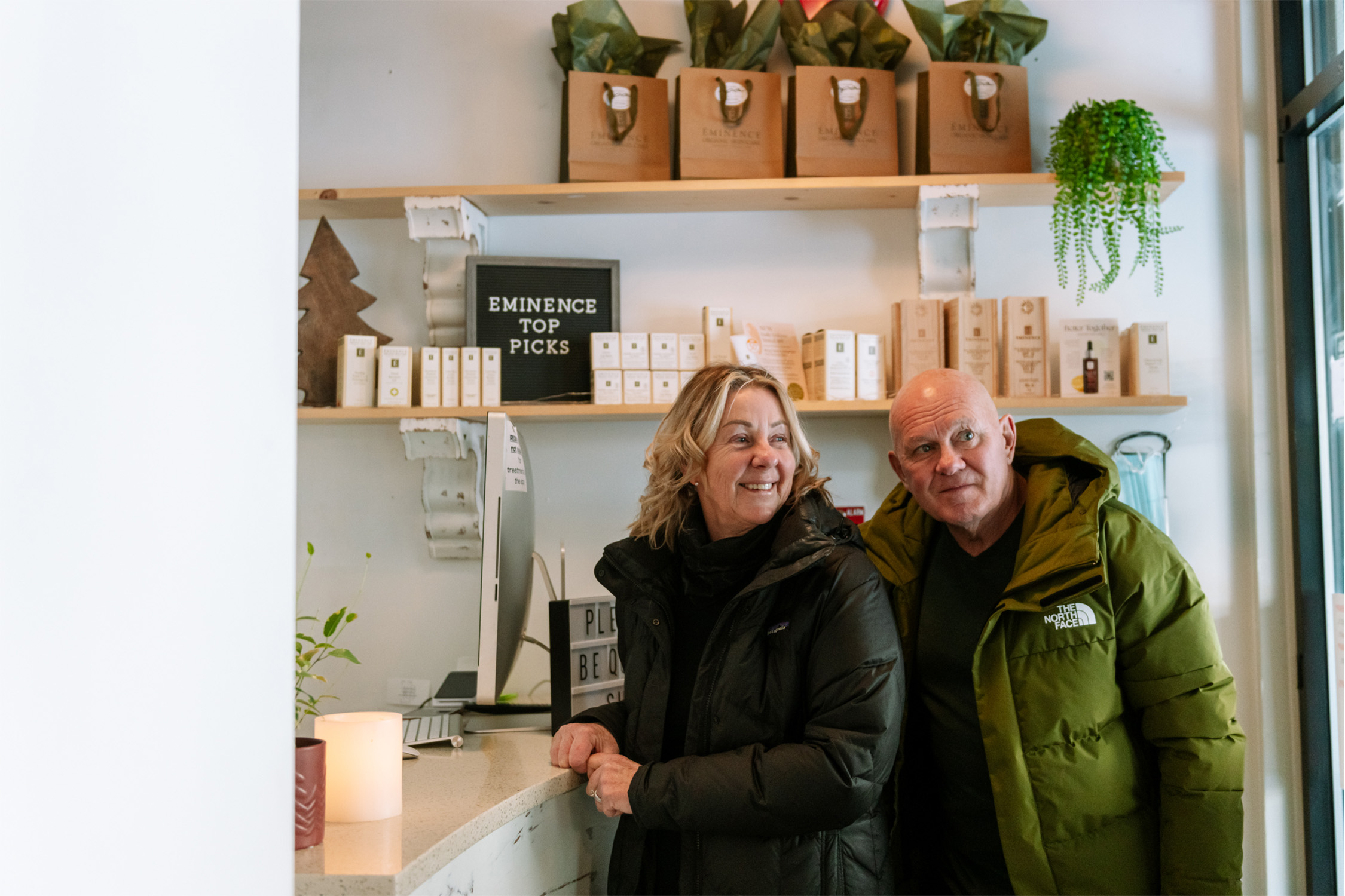 Couple smiles at the front desk of Sun Peaks Spa, with a glowing candle and spa products around.