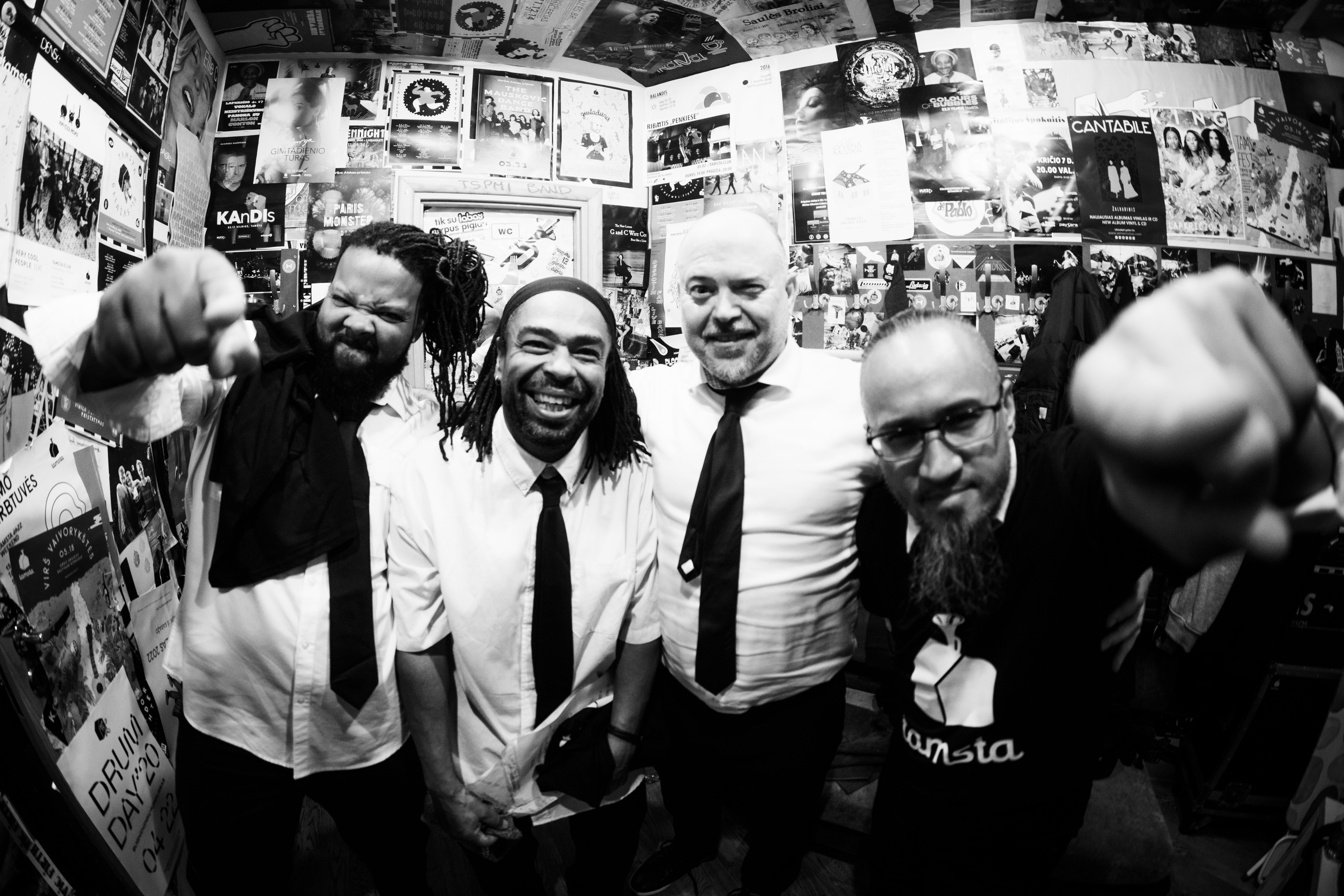 Four members of the musical group Tortured Soul smiling and pointing at the camera backstage. Black and white with fisheye effect.