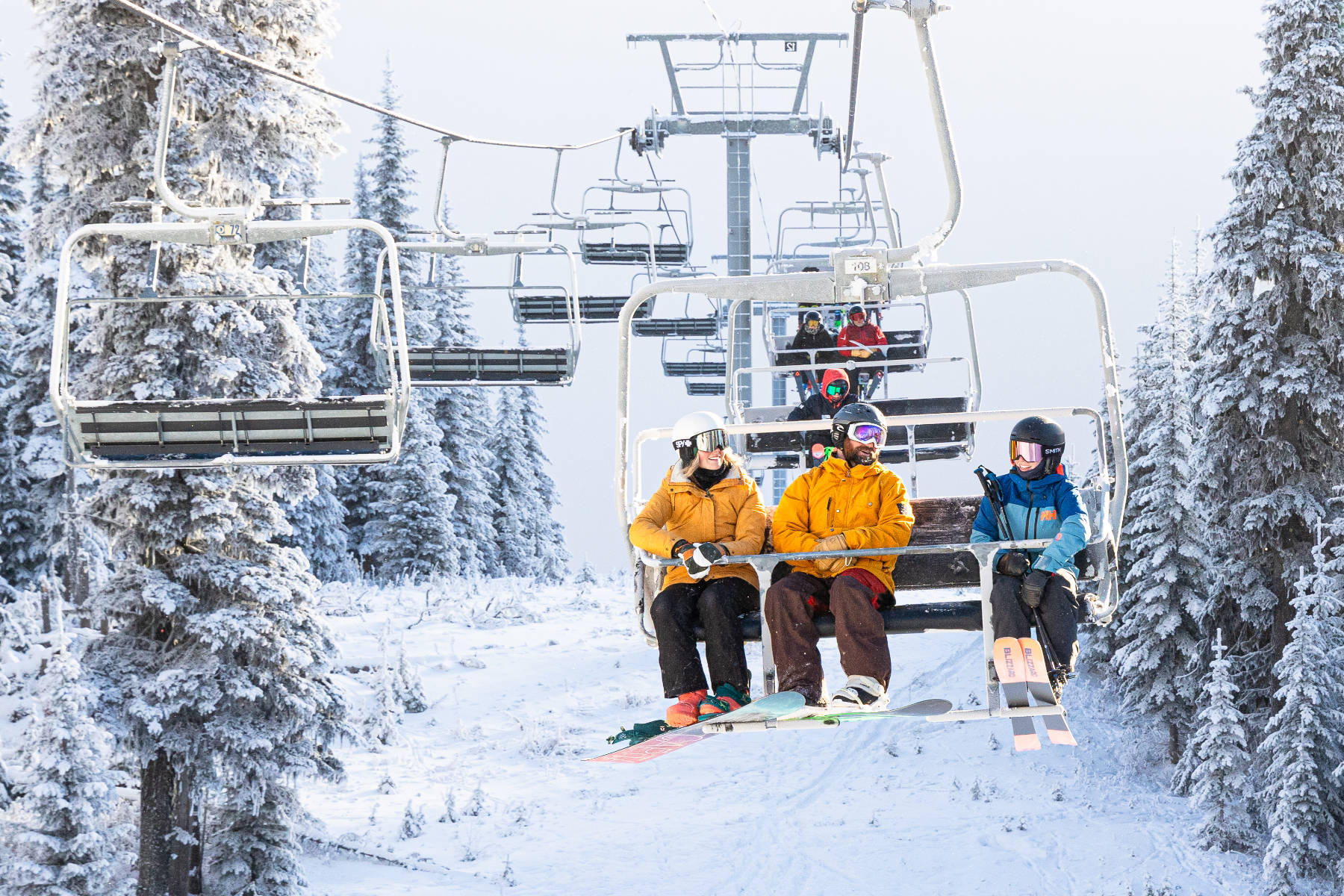 Three people sitting on a chairlift covered in snow with trees surrounding then