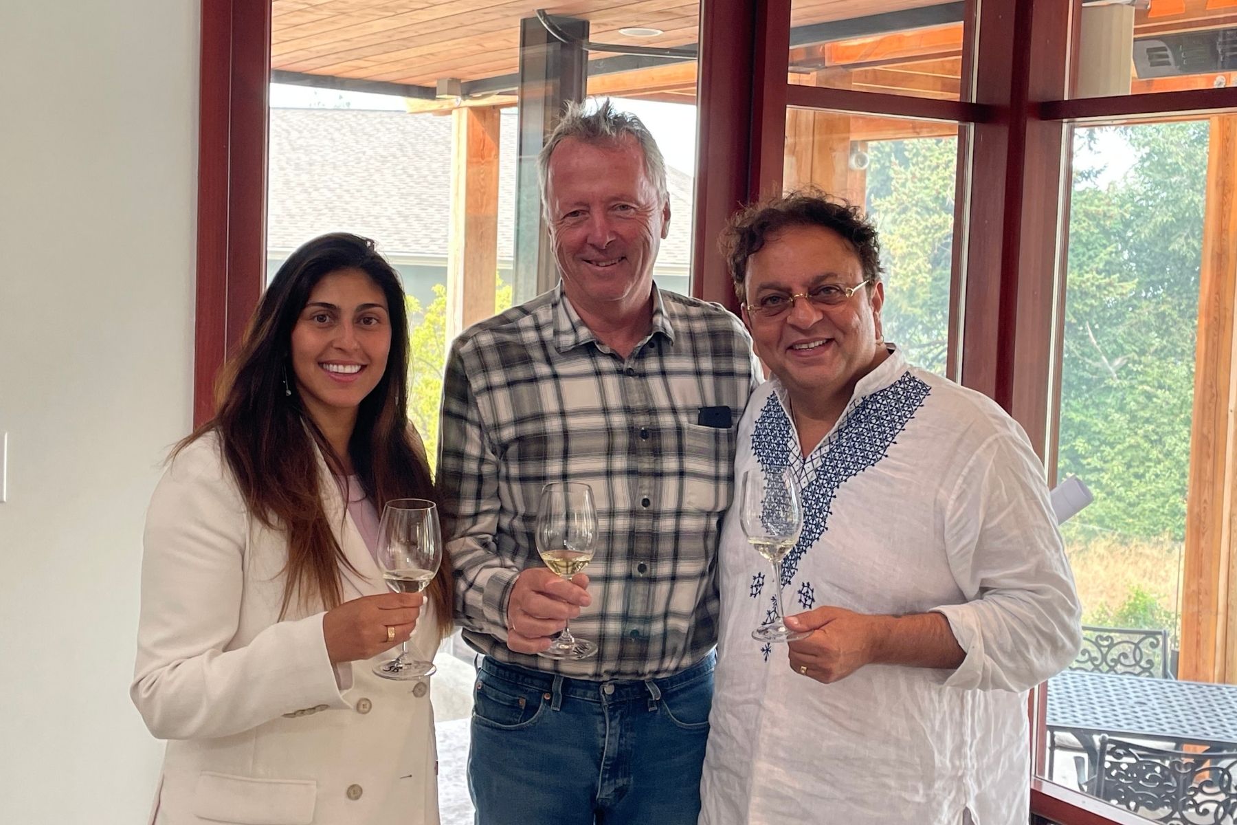 Three people including Vikram Vij tasting white wine and smiling inside a house.